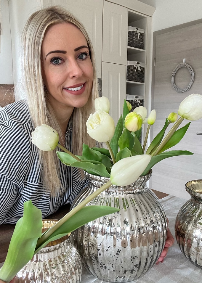 Frau mit blonden Haaren neben silberner Vase mit weissen Tulpen in modernem Interieur