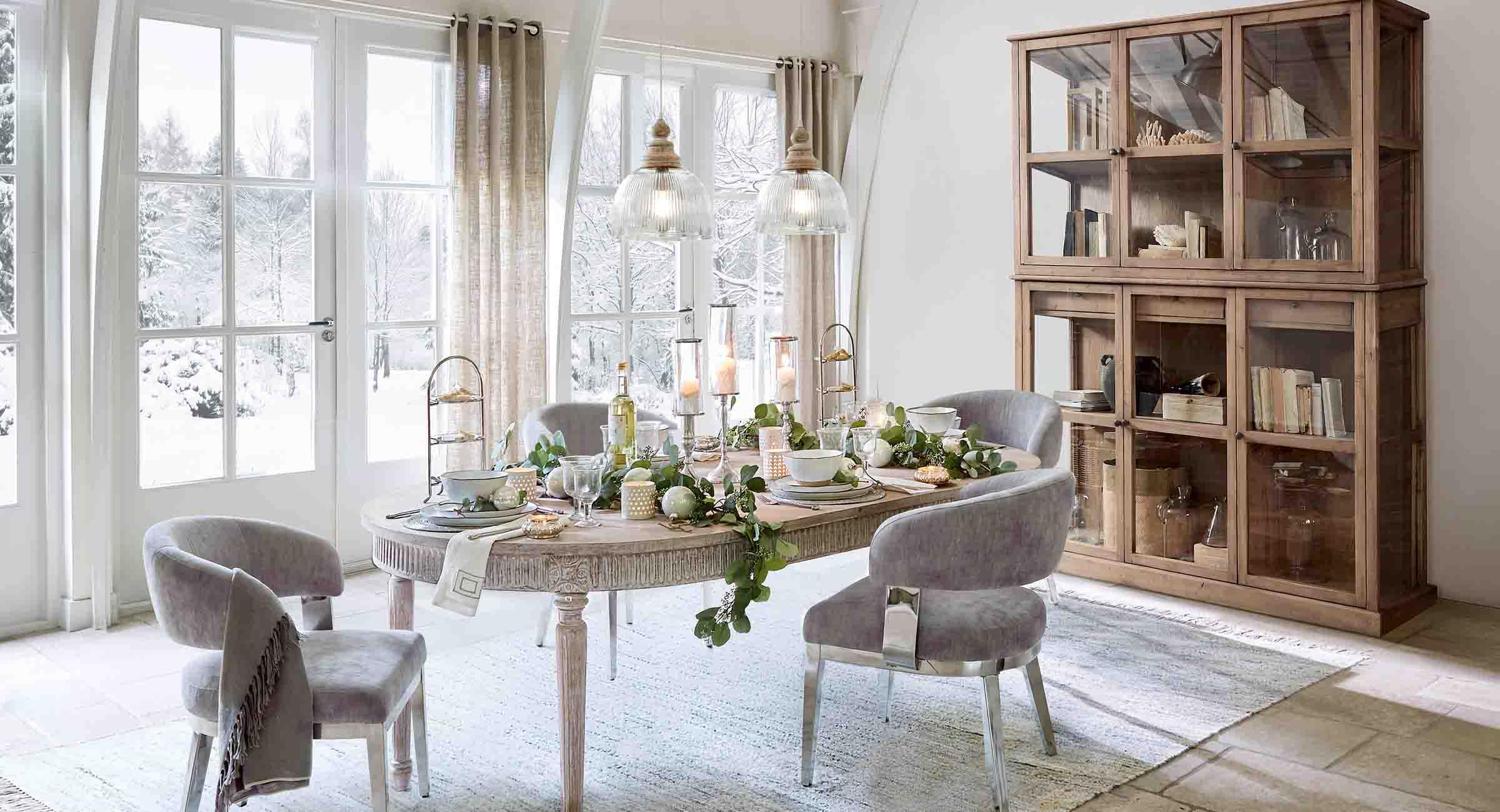 Esszimmer mit Holztisch und grauen Stühlen winterlich dekoriert mit Blick auf verschneiten Garten