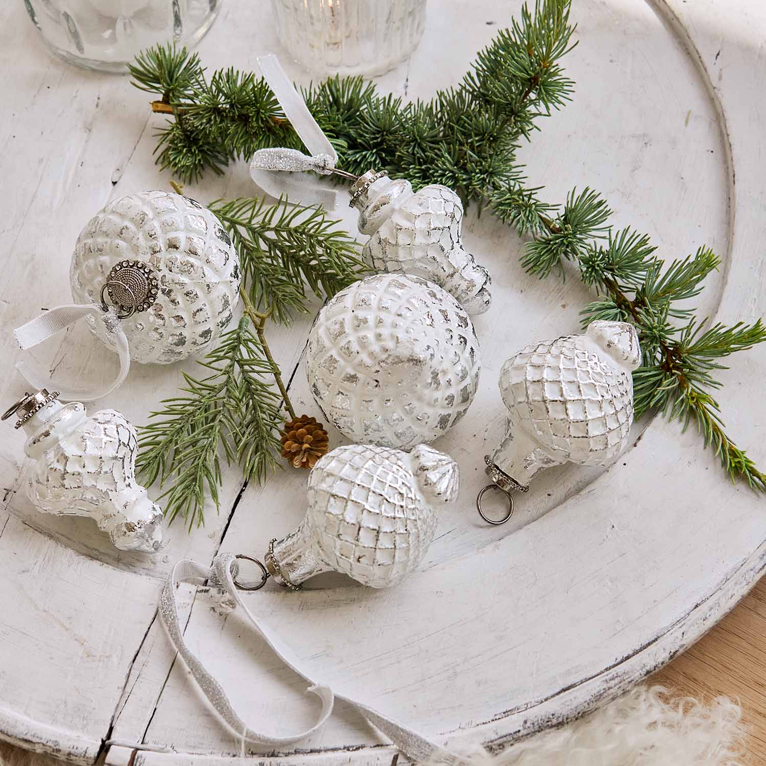 Weisse Weihnachtskugeln mit Rautenmuster auf Holztablett mit Tannenzweigen, festliche Dekoration