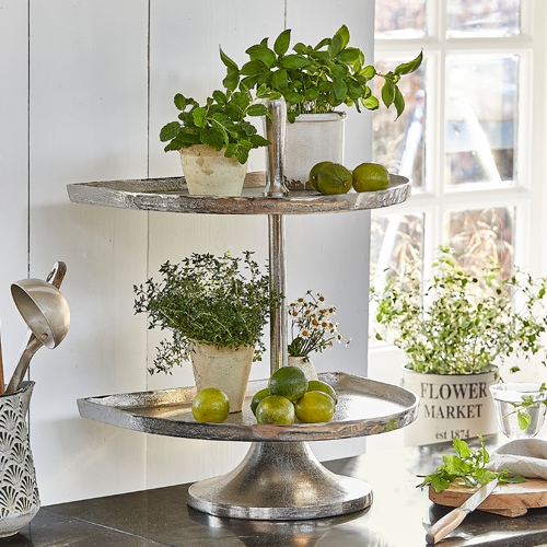 Zweistöckiges Tablett aus silbernem Metall mit Pflanzen und Limetten auf der Küchenarbeitsplatte