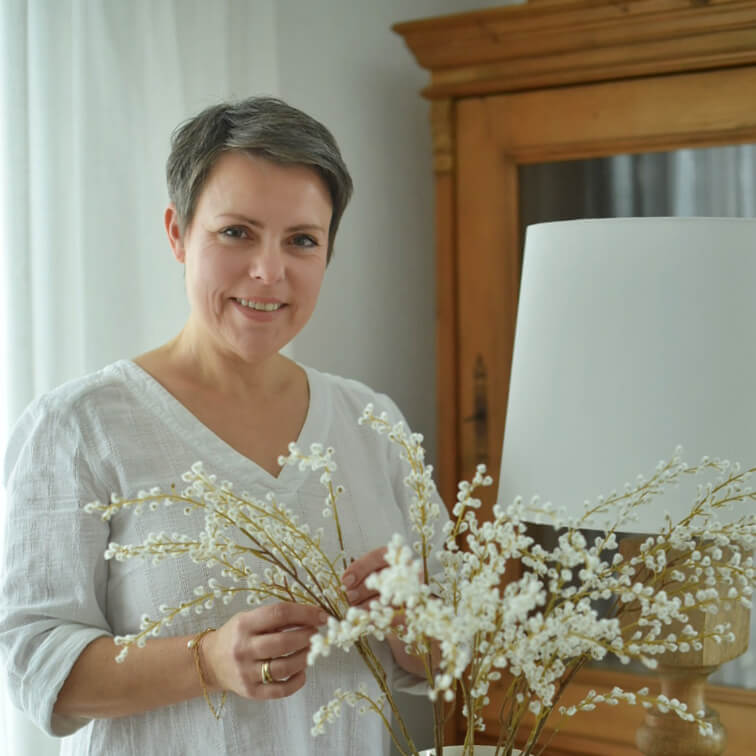 Frau in weisser Bluse hält dekorative Zweige mit weissen Blüten in hellem Raum