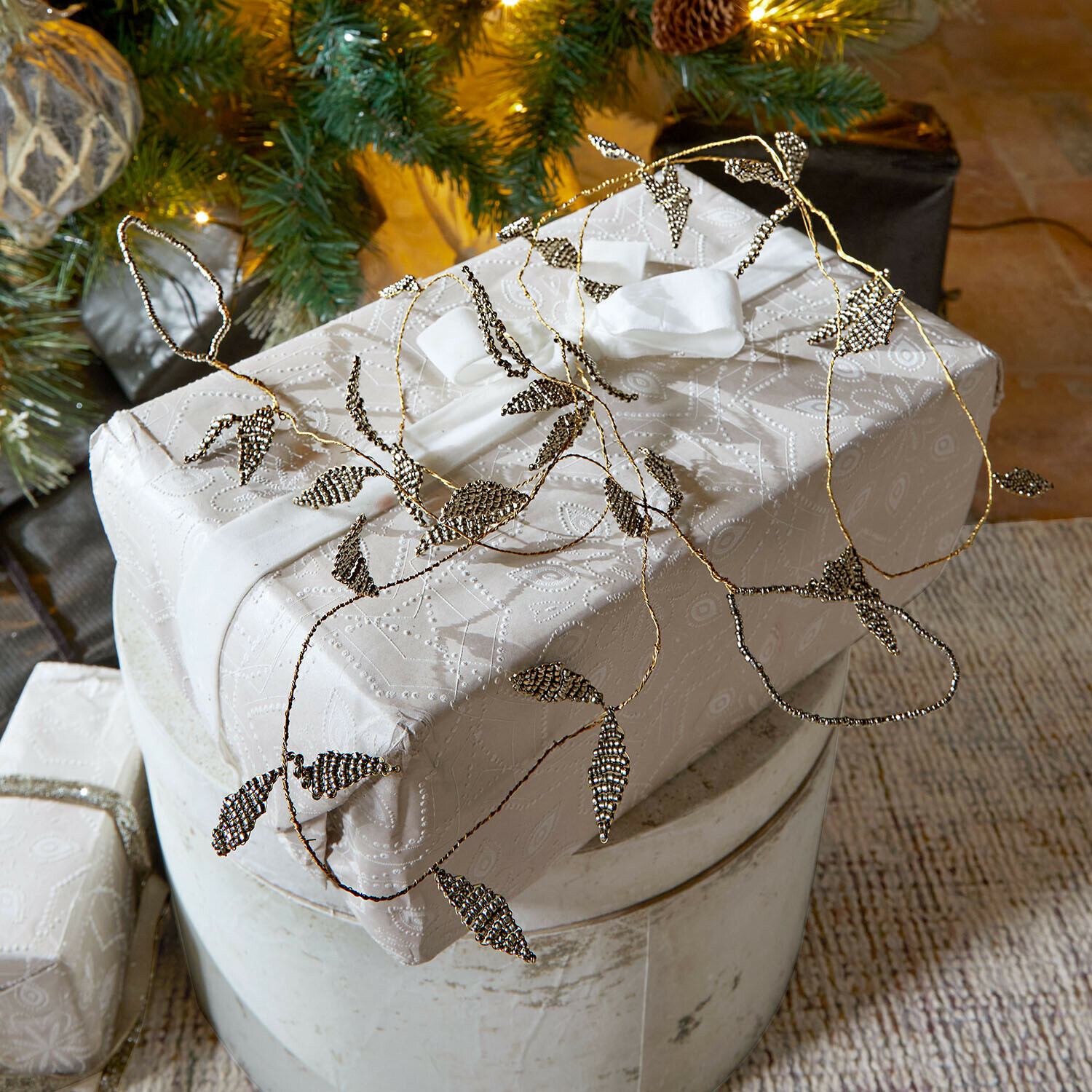 Girlande Laymira Elegantes Geschenk in weissem Papier mit feinem Muster und Metallblatt-Dekoration verpackt