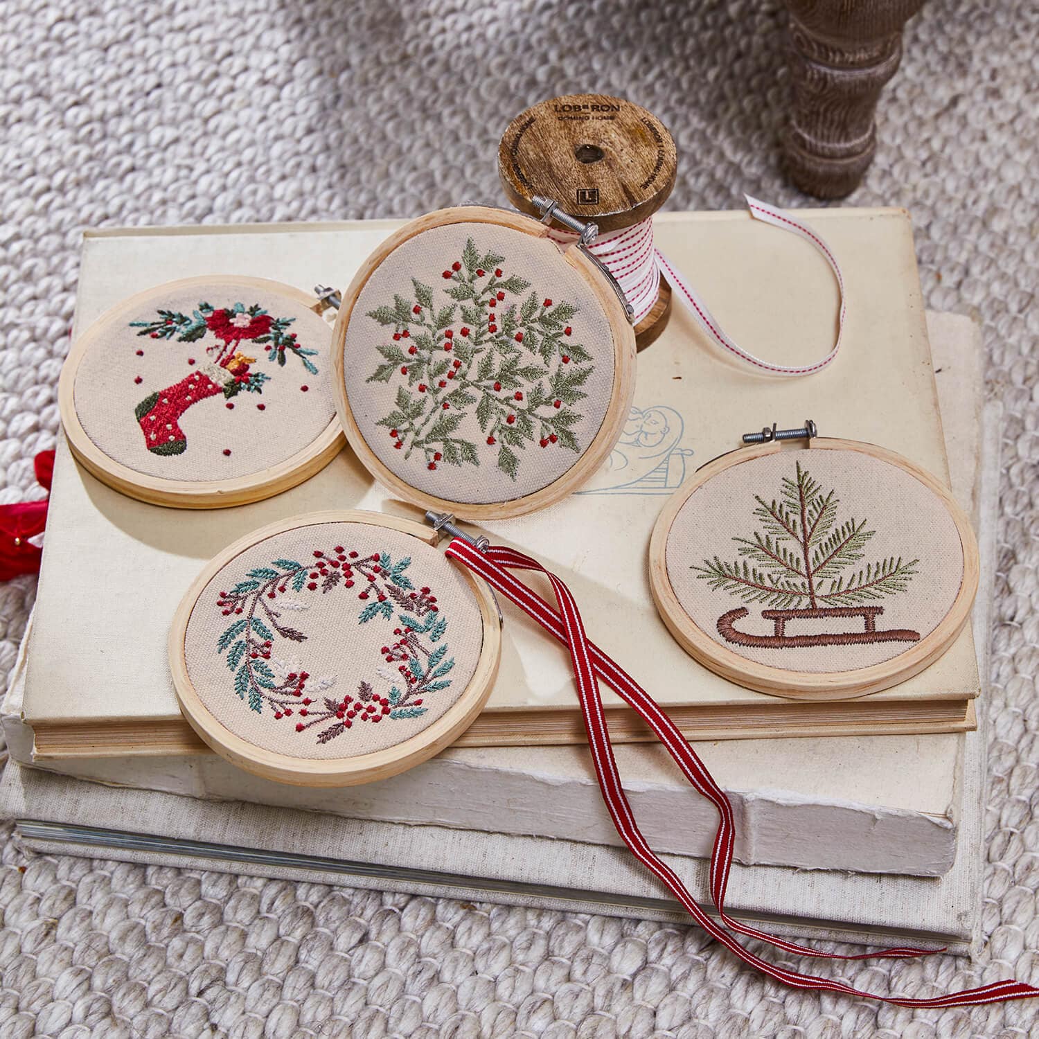 Set mit vier bestickten Weihnachtsanhängern mit pflanzlichen Motiven und roten Akzenten auf beigem Stoff