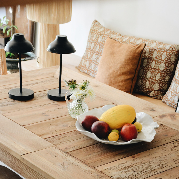 Holztisch mit dekorativer weisser Obstschale und zwei schwarzen Tischlampen in gemütlichem Raum