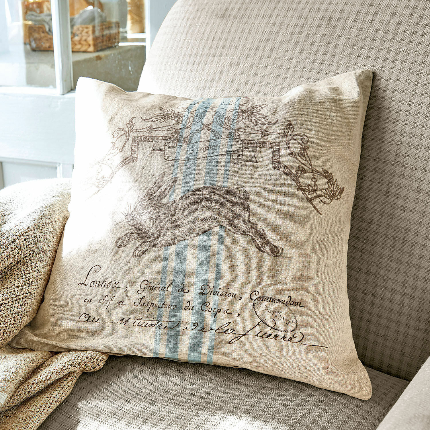 Kissenhülle La Lapin Beiges Leinenkissen mit Hasenmotiv und blauen Streifen auf grauem Sofa, Wohnaccessoire
