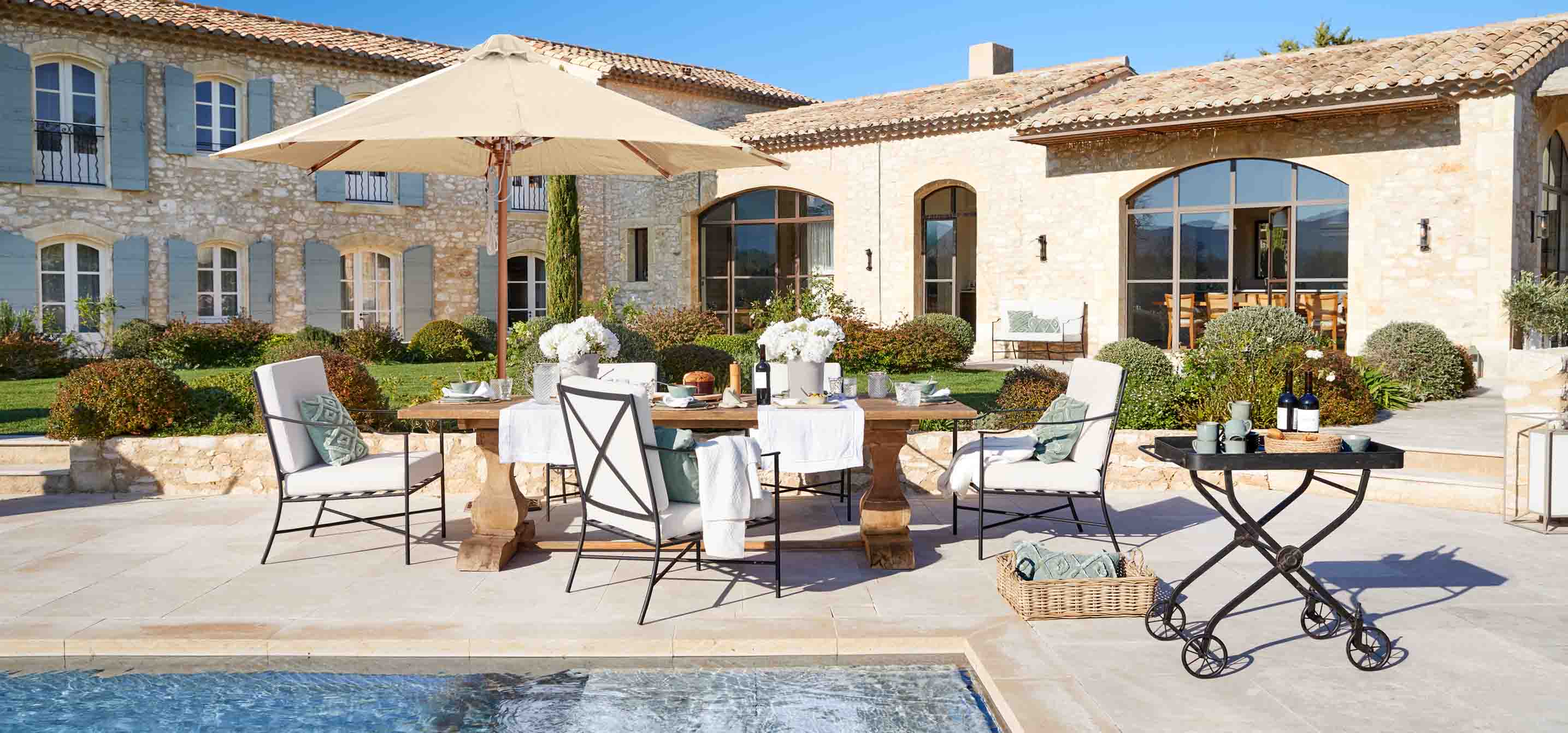 Gartenmöbel-Set mit Holztisch und cremefarbenen Polstern am Pool im rustikalen Stil
