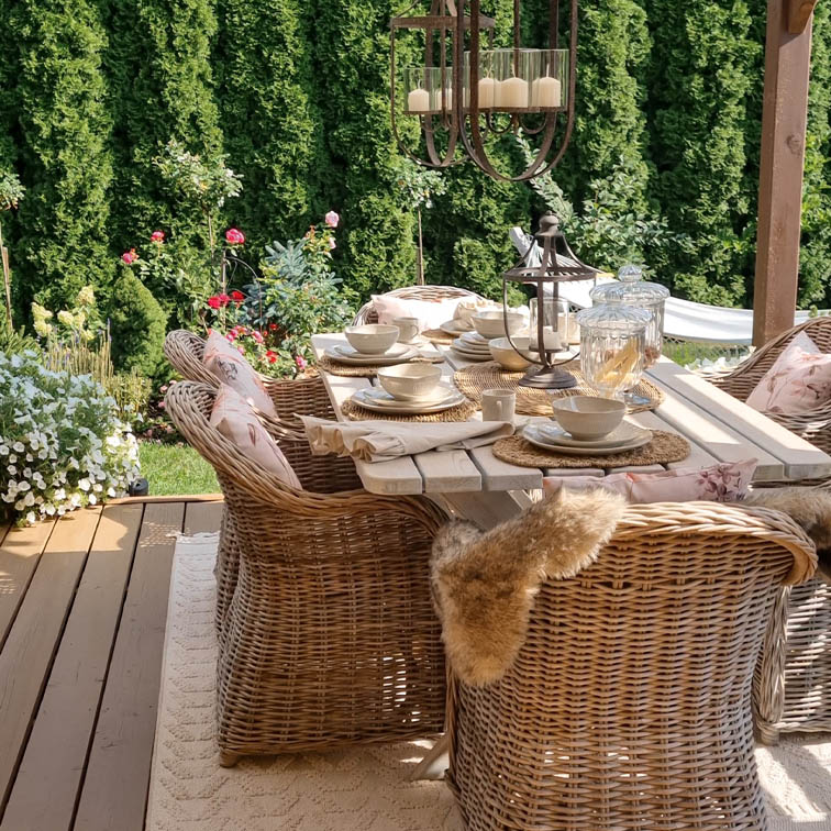 Gartenmöbel-Set aus natürlichem Rattan mit weissem Tisch und Dekorationen auf sonniger Terrasse
