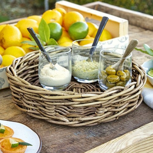 Runder Weidenkorb mit drei Gläsern und Löffeln auf Holztisch mit Zitrusfrüchten