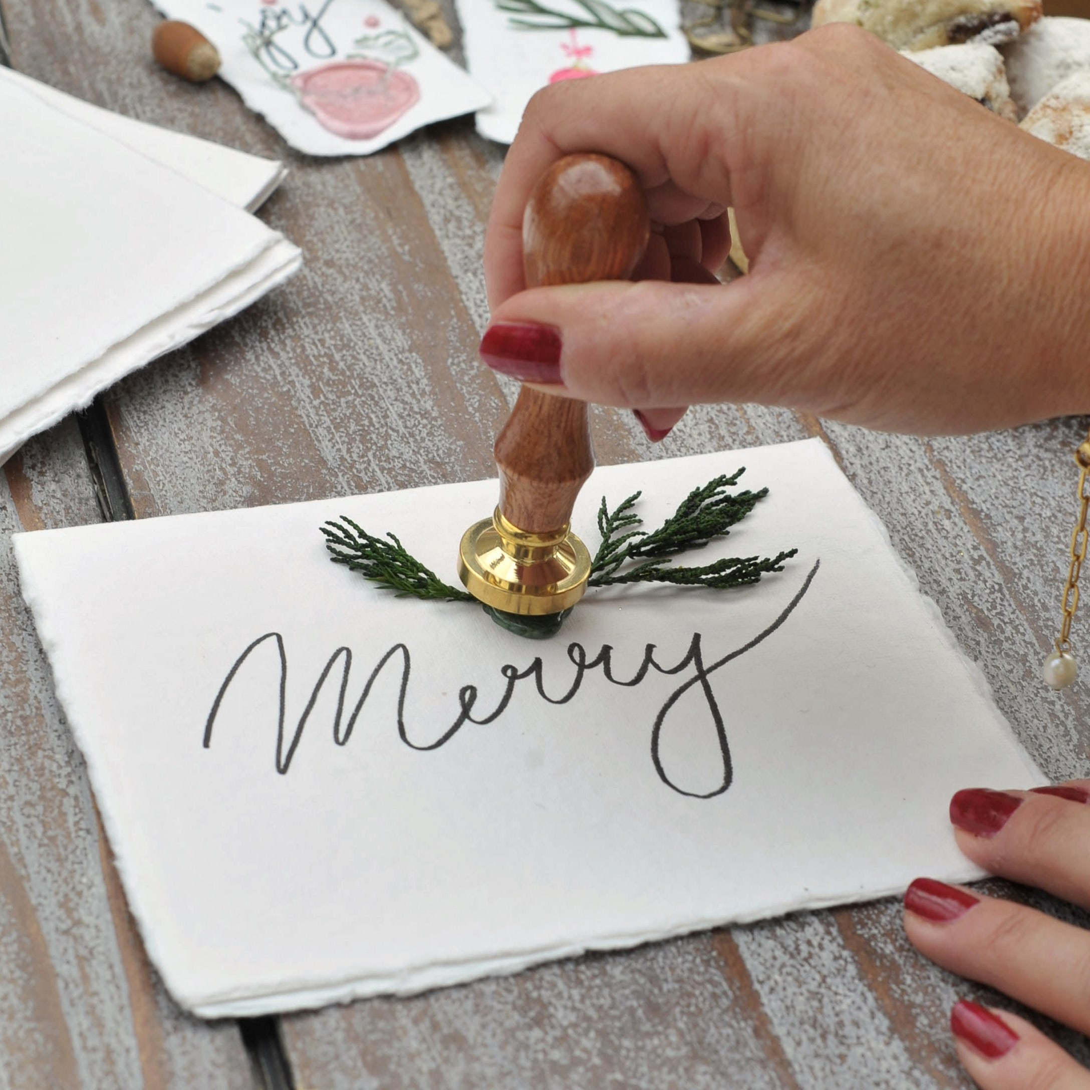 Holzstempel zum Verzieren von Geschenken auf weisser Karte mit Schriftzug «Merry» und grünen Zweigen