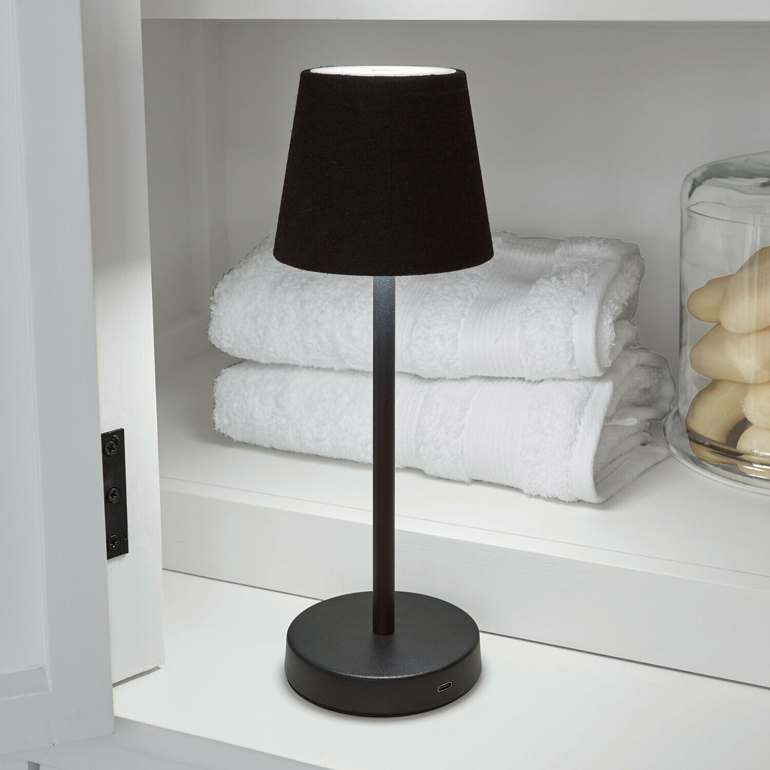 Wiederaufladbare Tischlampe Sylvainie Schwarze Tischlampe mit Stoffschirm auf Metallfuß neben weissen Handtüchern