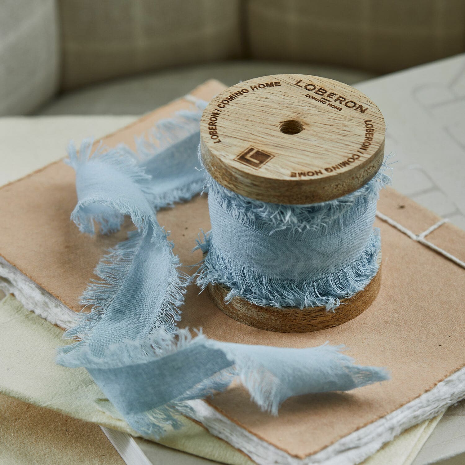 Band Celoria Hellblaues Baumwollband mit ausgefransten Kanten, auf einer Holzspule liegend, auf Notizbüchern