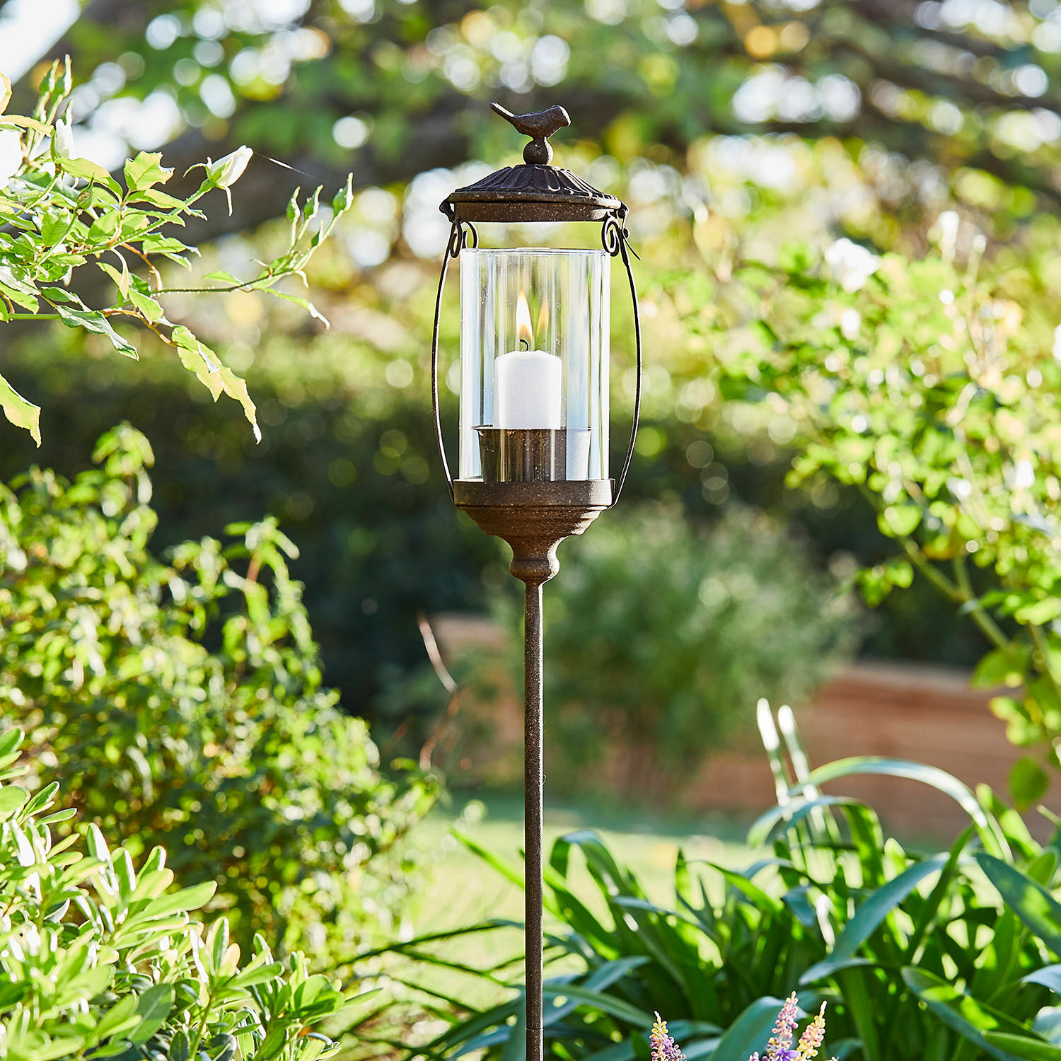 Laterne Nexoril Metall-Gartenlaterne mit weisser Kerze und Glaszylinder vor grünem Pflanzenhintergrund