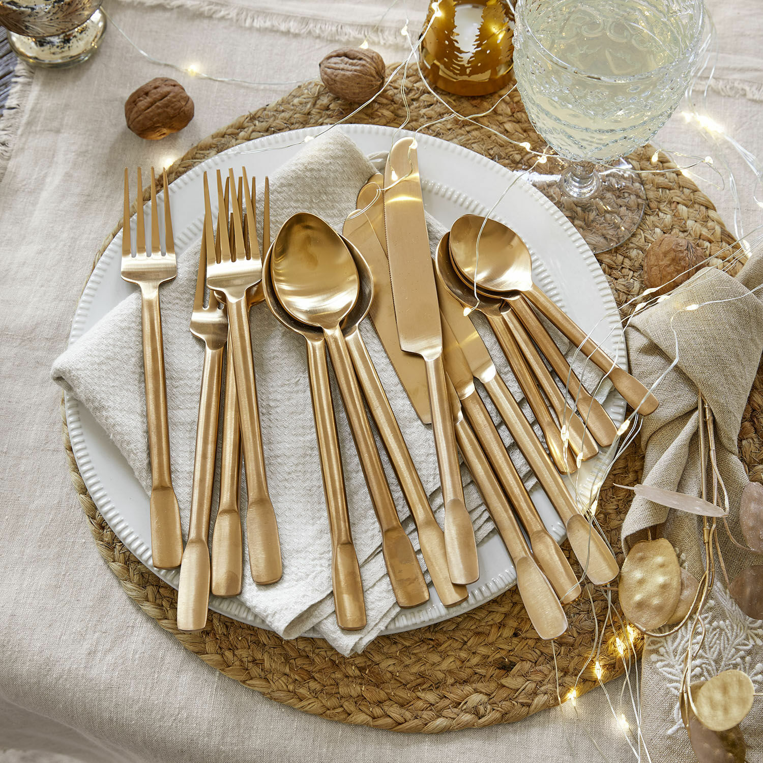 Besteck Malroy Set goldfarbener Edelstahlbestecke auf weissem Teller mit festlicher Dekoration und LED-Lichterkette