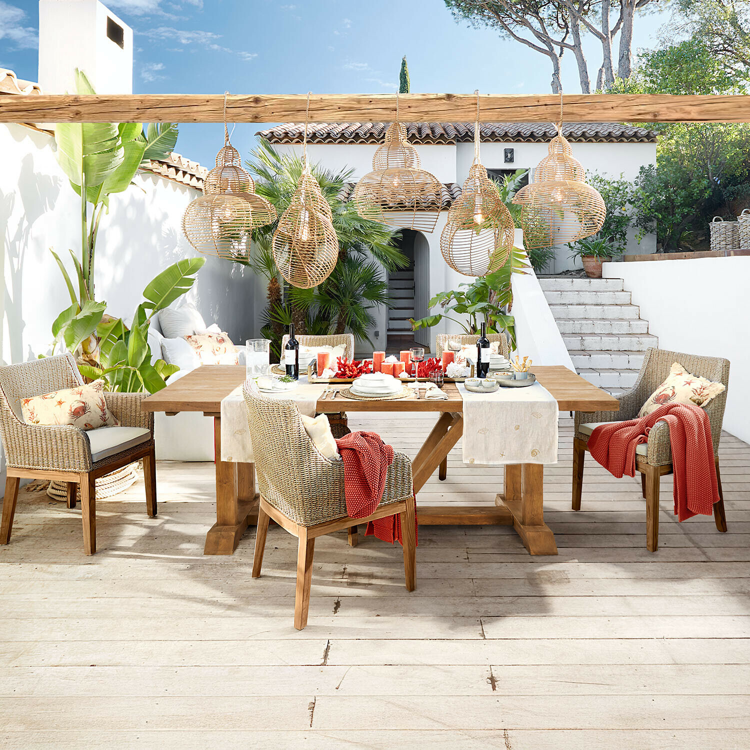 Tisch Melvoro Gartenmöbel aus Holz und Rattan in Naturfarben mit hängenden Korblampen auf Terrasse