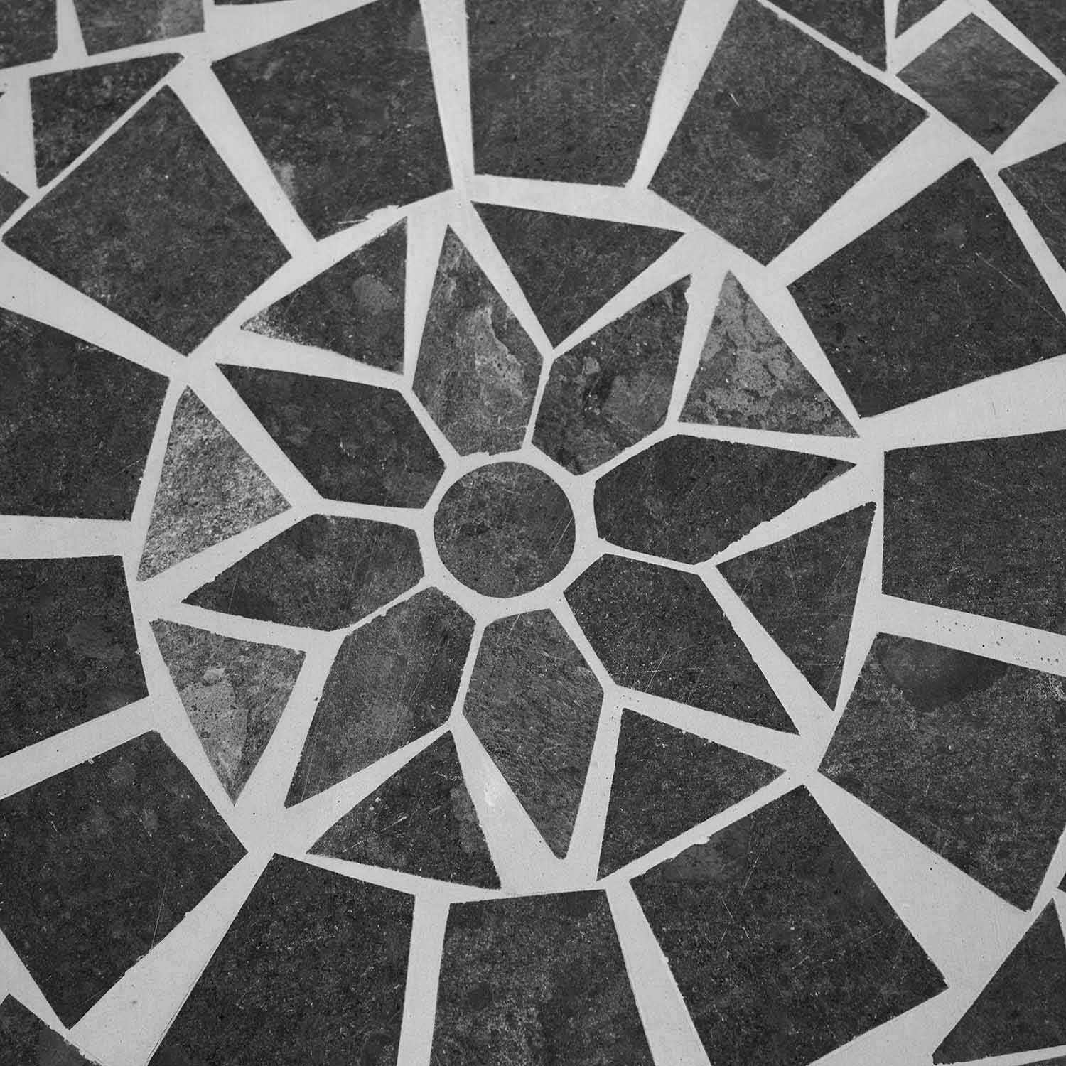 Mosaik aus dunkelgrauen Steinplatten in geometrischem Blumenmuster auf hellem Untergrund