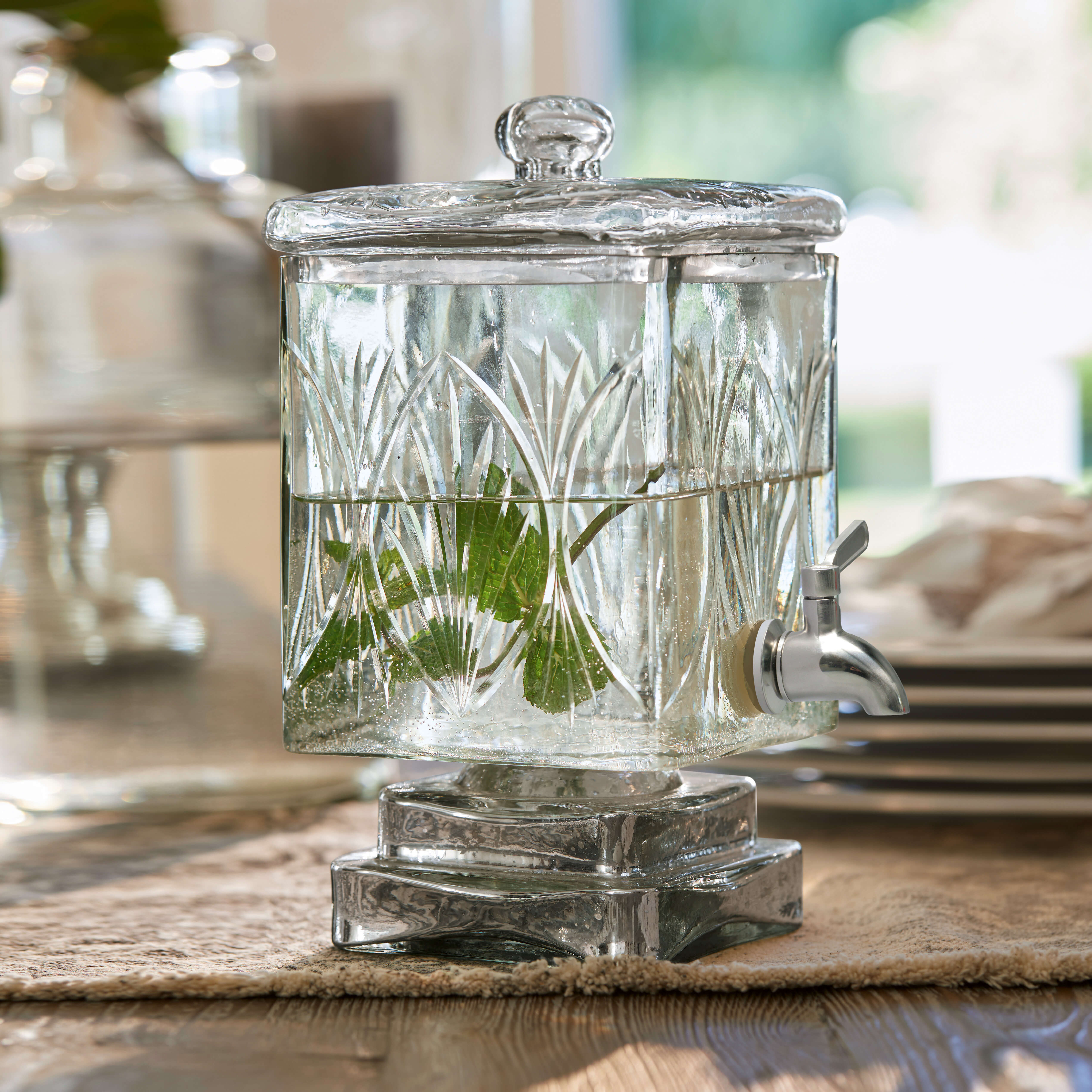 Glas-Getränkespender mit Deckel und Zapfhahn, transparent mit grünen Blättern, dekorativ