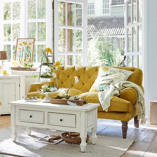 Gelbes Samtsofa im Vintage-Stil im hellen Wohnzimmer mit weissem Holztisch und Dekorationen