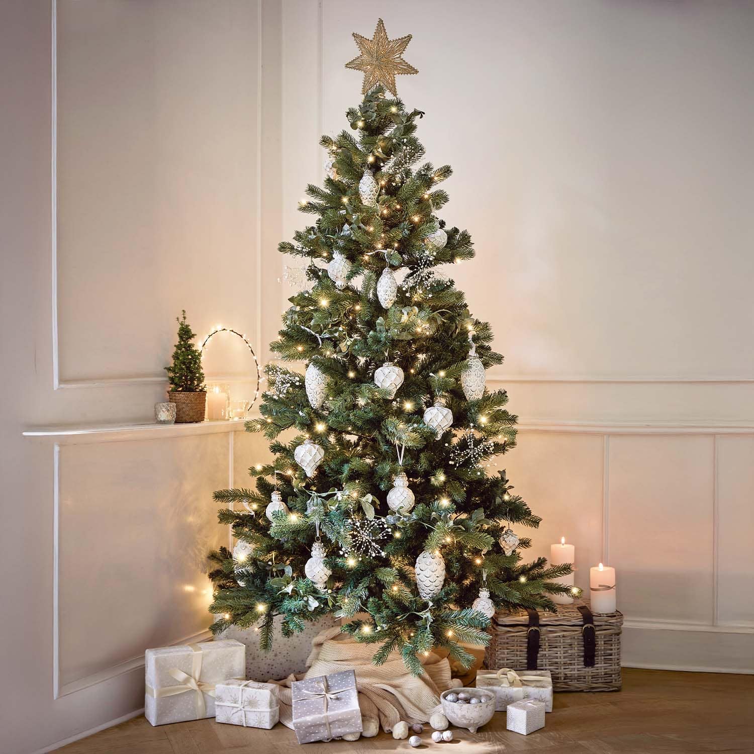 Weihnachtsbaum mit weissen Kugeln und Lichterkette geschmückt, Geschenke und Kerzen in gemütlichem Raum