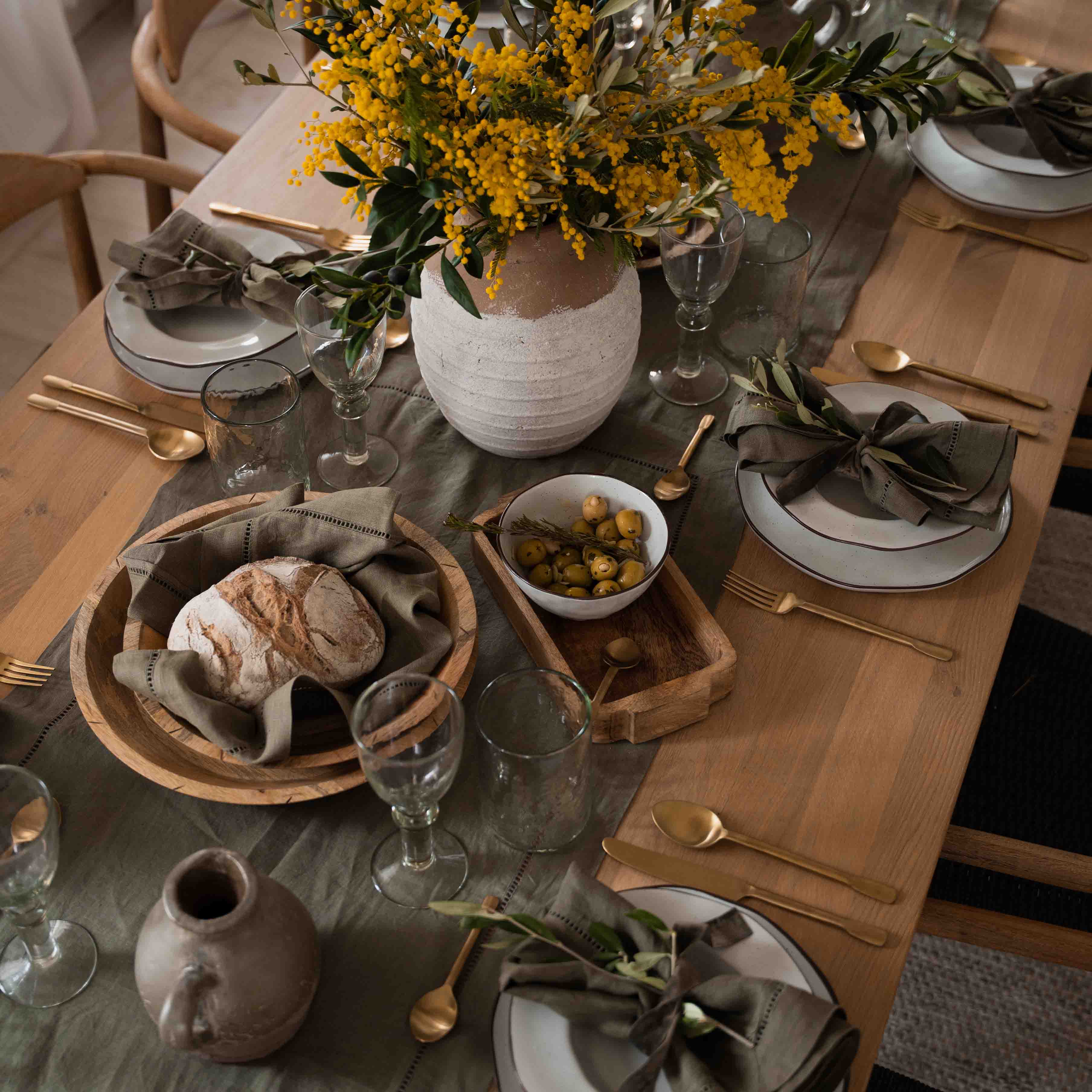 Rustikaler Holztisch mit weissem Geschirr, grünen Servietten und gelbem Blumenstrauss in Tonvase