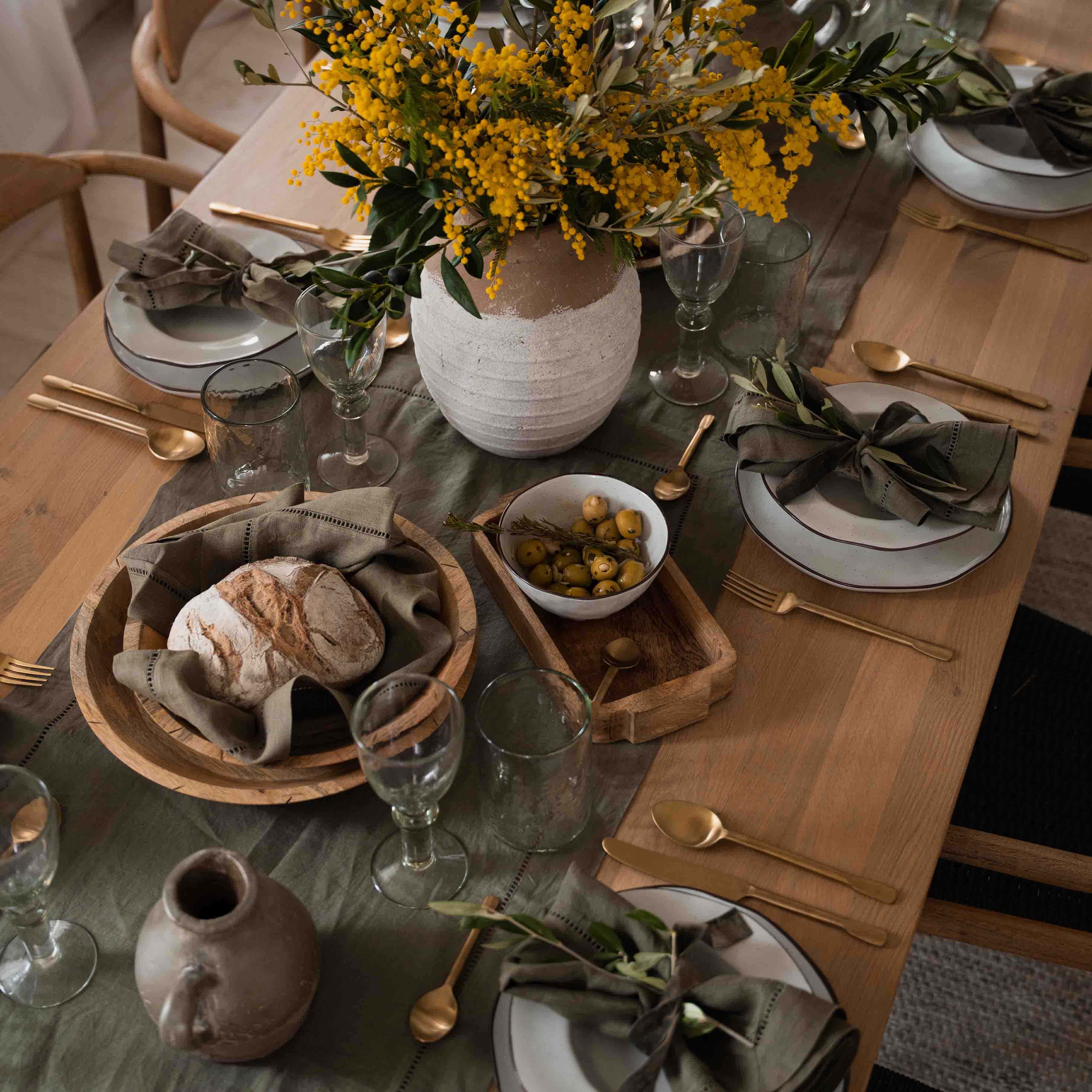 Rustikaler Holztisch mit weissem Geschirr, grünen Servietten und gelbem Blumenstrauss in Tonvase