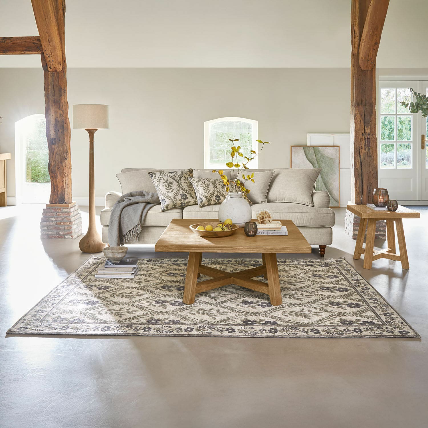 Gemütliches Wohnzimmer mit beigem Sofa, Holzcouchtisch und Teppich mit Pflanzenmuster.