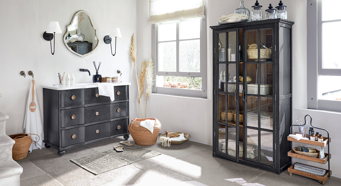 Helles Badezimmer mit schwarzer Kommode und Glastürenschrank, natürlichen Accessoires und Tageslicht.