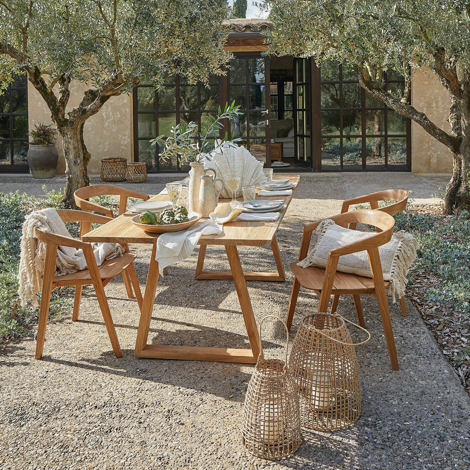 Tisch Saulny Gartenmöbel-Set aus natürlichem Teakholz mit Dekorationen und Laternen auf der sonnigen Terrasse