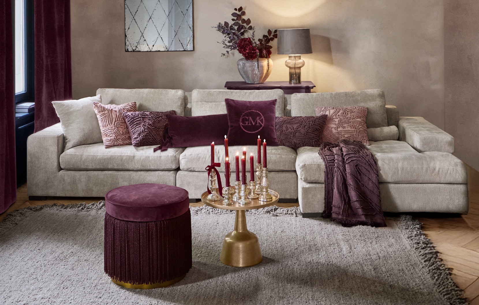 Beiges Sofa mit violetten Kissen und bordeauxfarbenem Hocker in stilvollem Wohnzimmer mit Kerzen