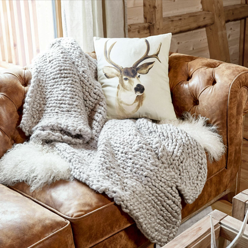 Dicke graue Wolldecke auf braunem Ledersofa mit Kissenmotiv Hirschkopf