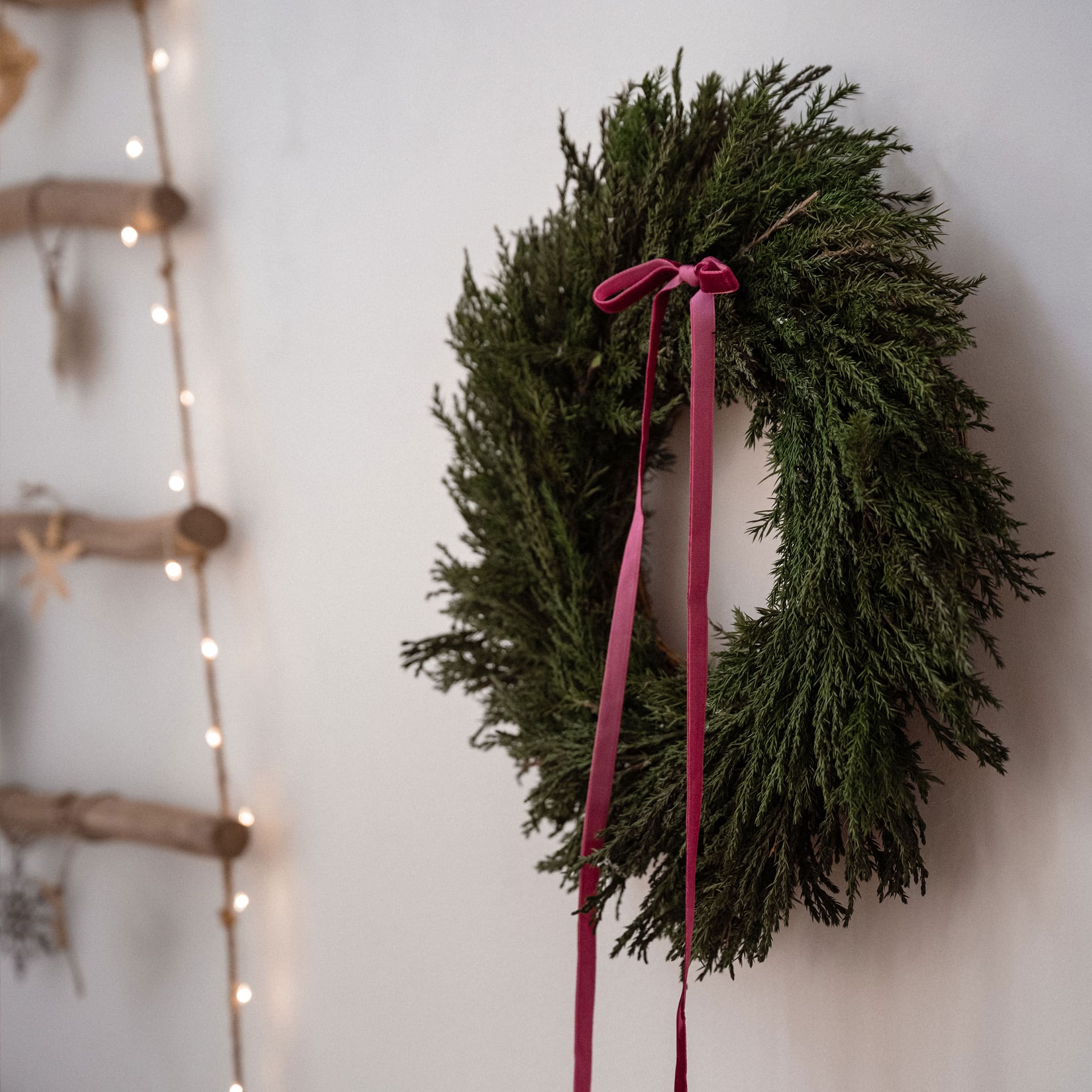 Weihnachtskranz aus grünen Zweigen mit rosa Schleife an weisser Wand, festliche Dekoration