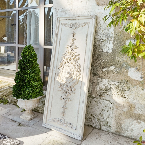 Weisses dekoratives Holzpaneel mit Vintage-Relief vor einer Steinmauer neben einer grünen Pflanze