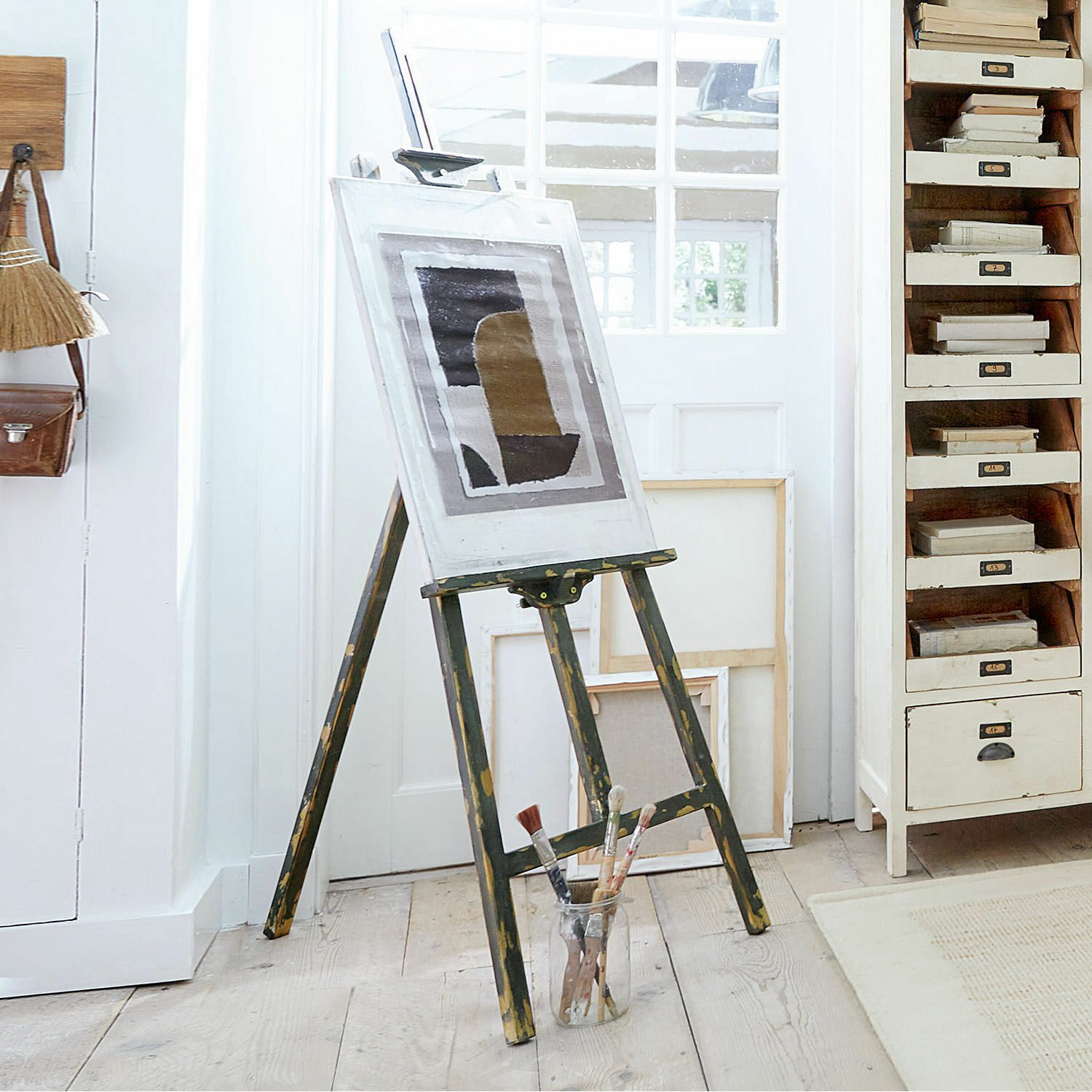 Staffelei Arabella Vintage-Holzmalstaffelei mit Bild und Pinseln auf hellem Holzboden im Atelier
