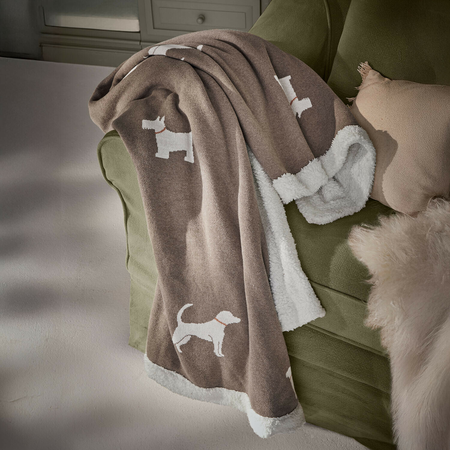 Hundedecke Olyden Braune Kuscheldecke mit weissem Teddyfutter und weissen Hundemotiven auf grünem Sofa