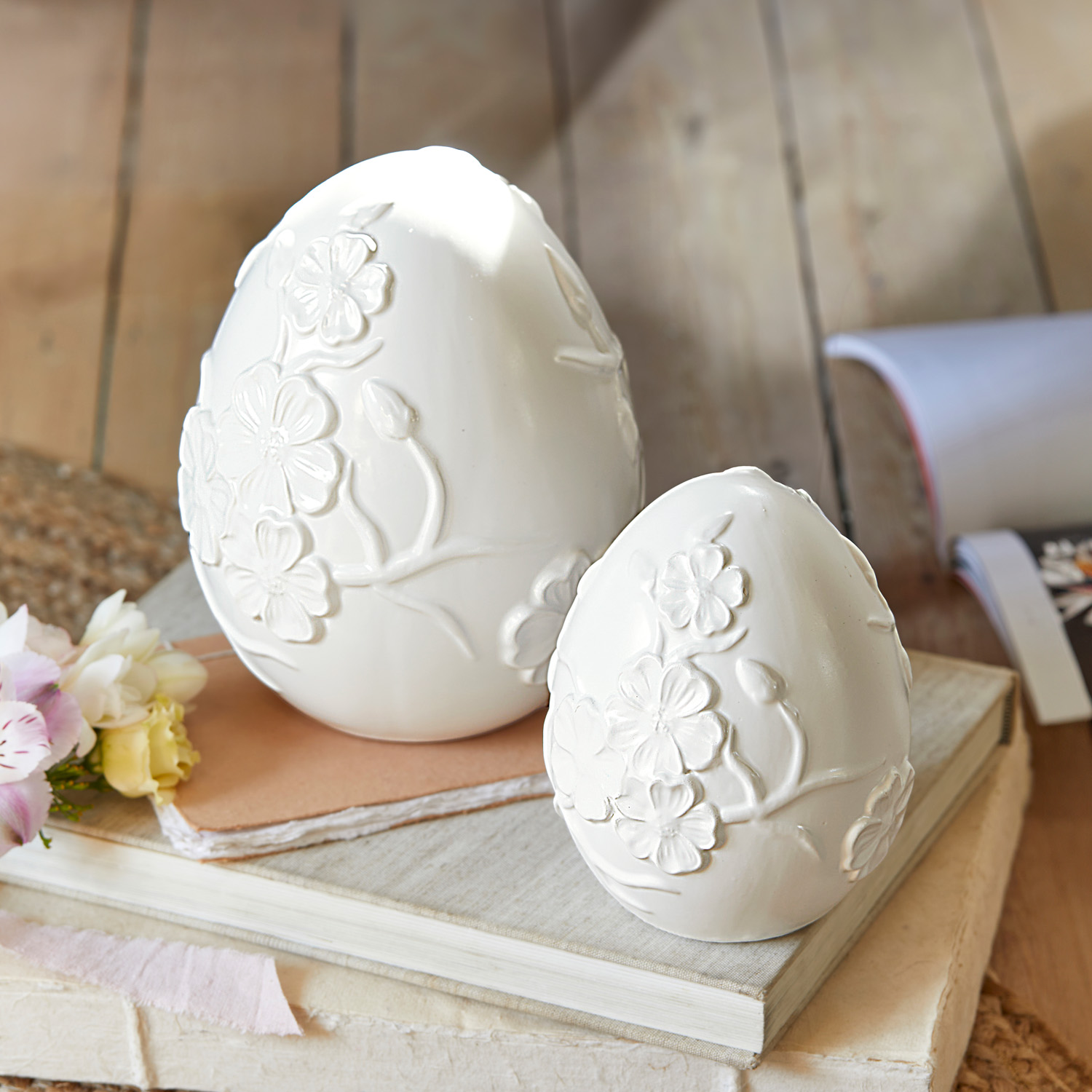 Weisse Keramik-Eier mit Blumenrelief auf Büchern, dekorative Frühlingsdekoration