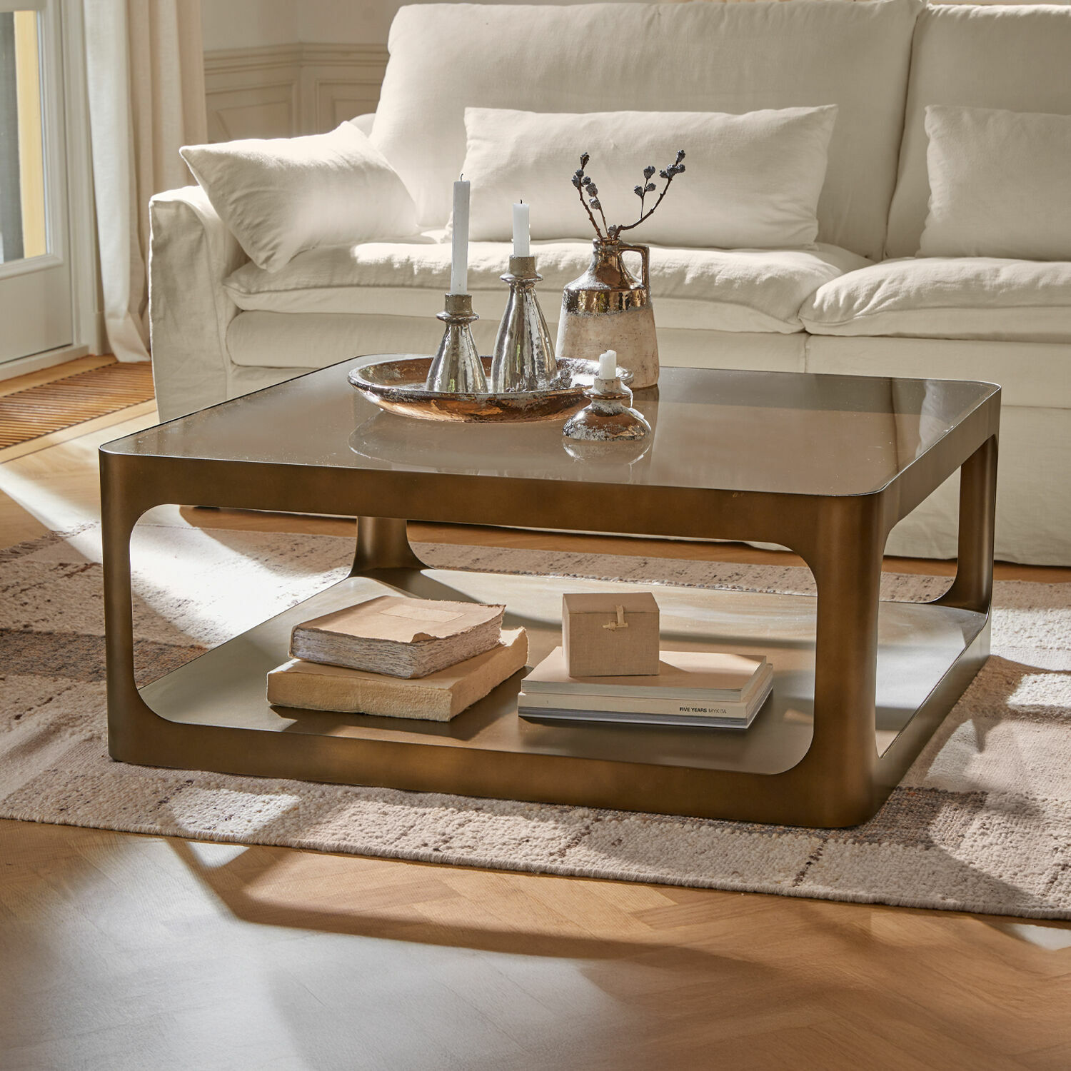 Couchtisch Bexington Quadratischer Couchtisch aus Metall in Messingfarbe mit Ablage und Dekoration auf hellem Teppich