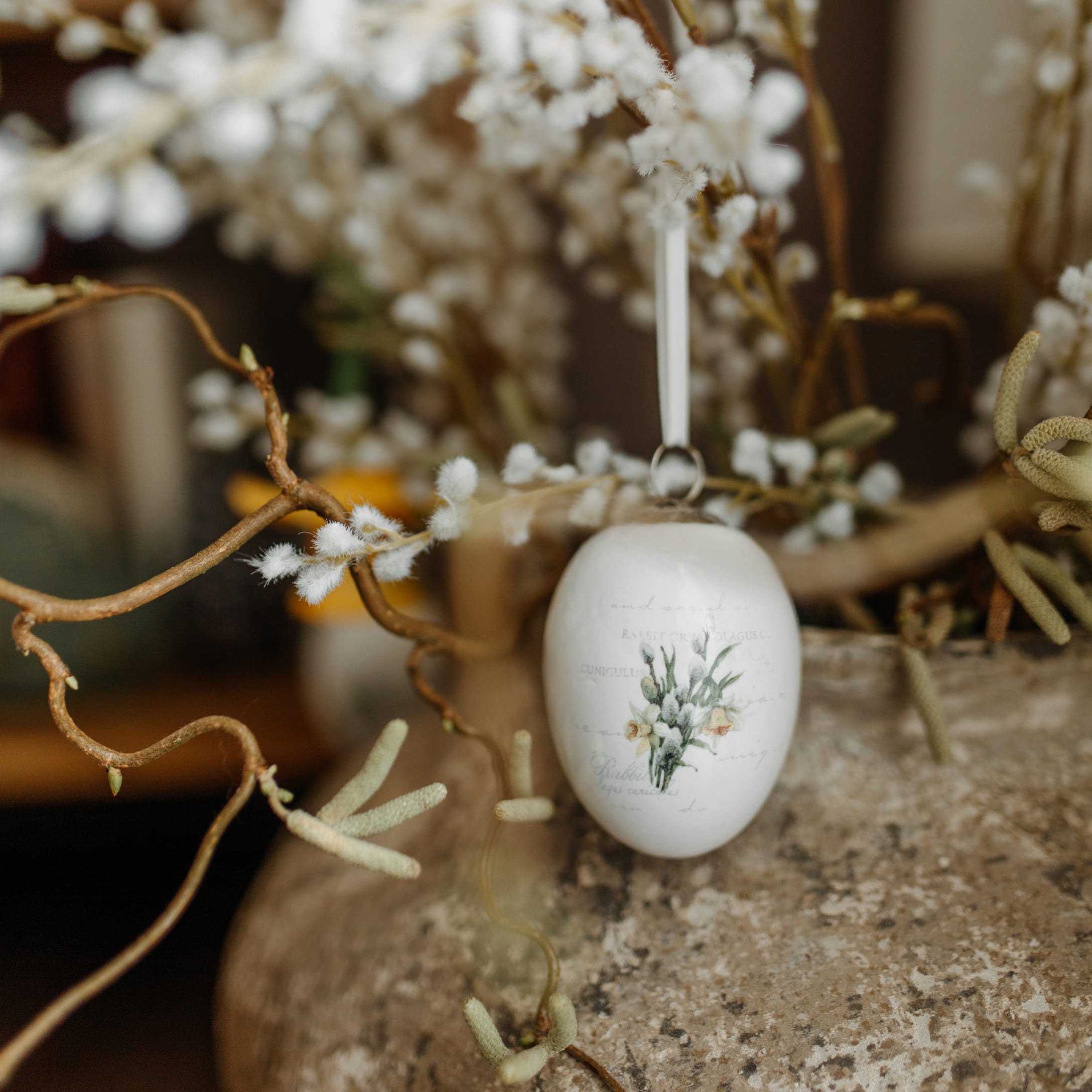 Weisse Keramik-Ostereier-Dekoration mit Blumenmotiv an dekorativem Zweig hängend