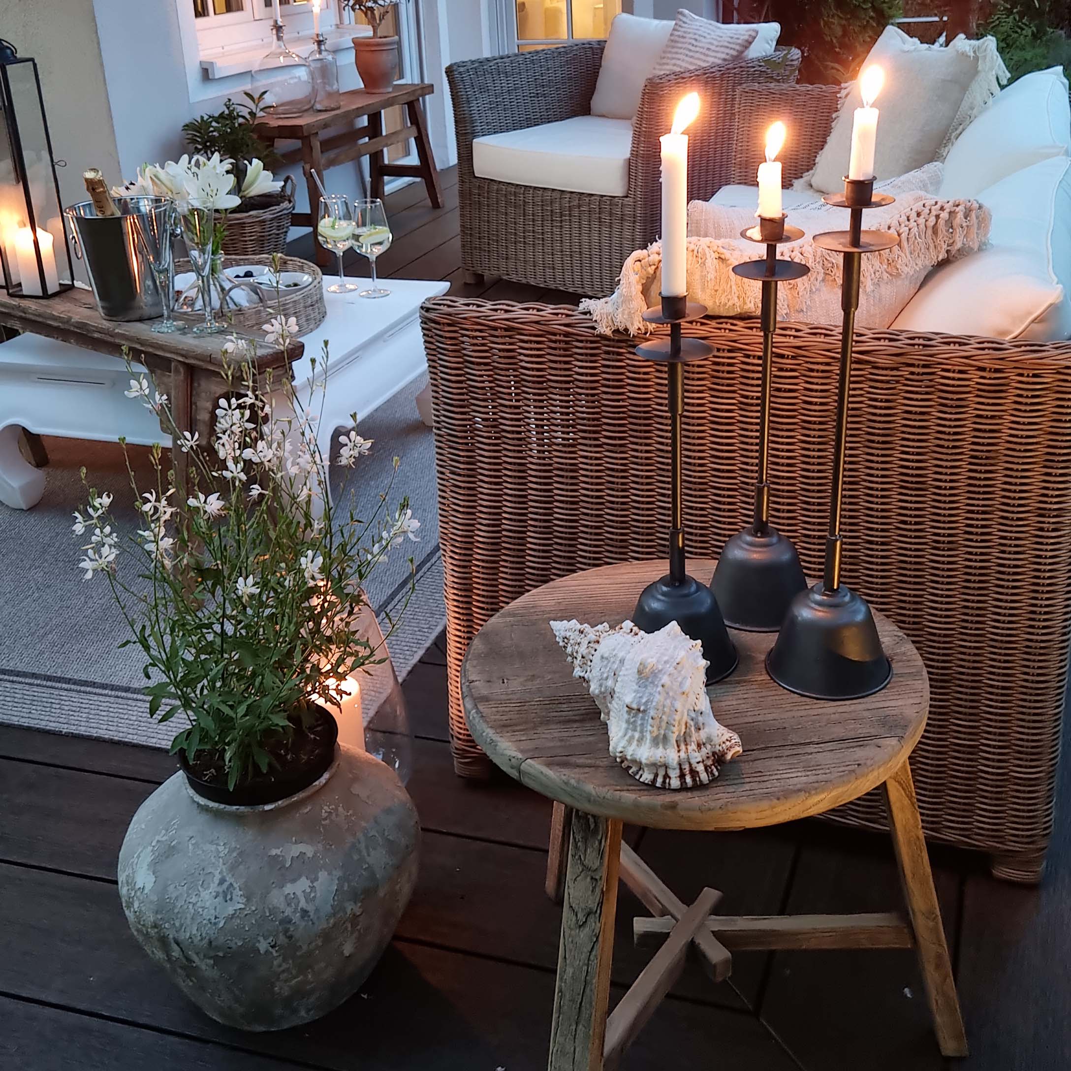 Gemütliche Terrasse mit Rattansofa, Holztisch und schwarzen Metallkerzenhaltern mit weissen Kerzen