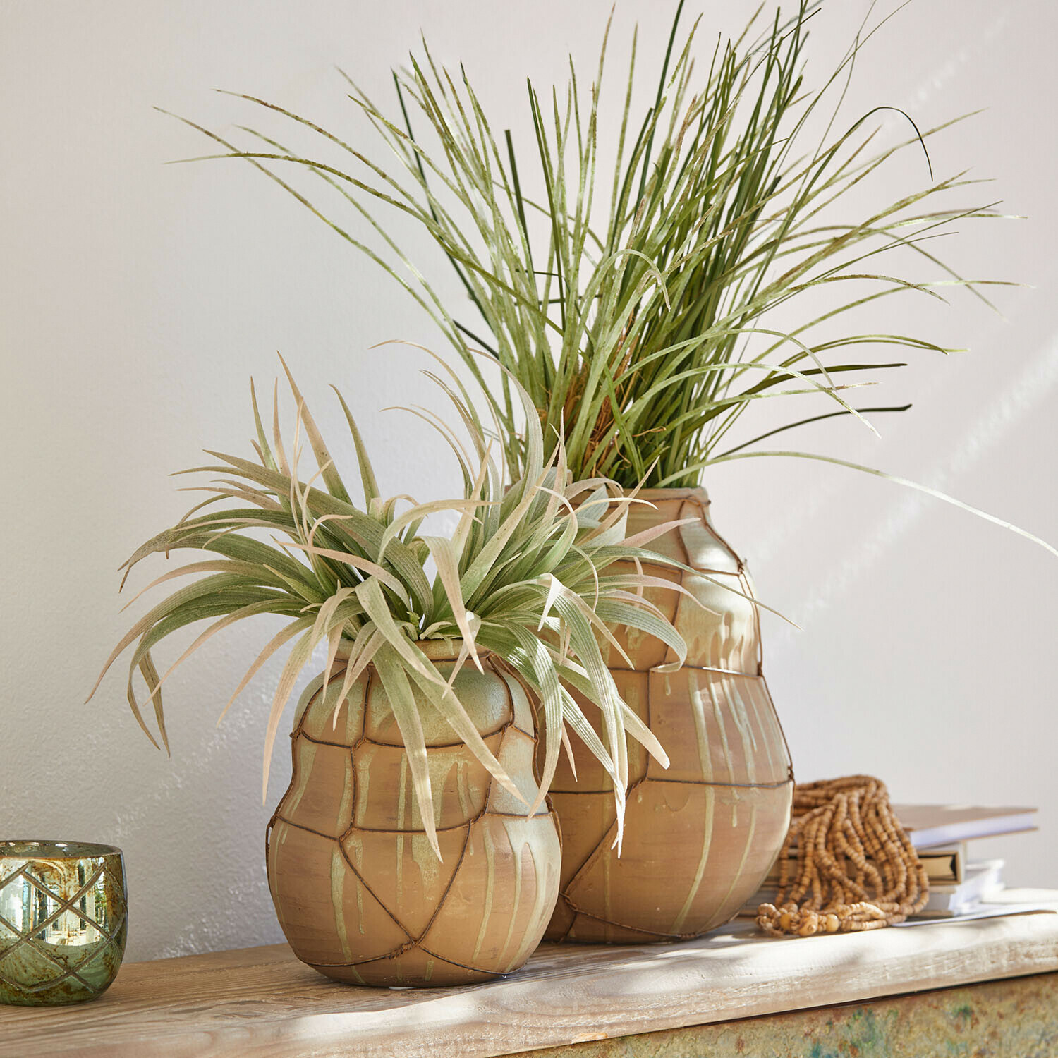 Zwei beige Keramikvasen mit grünen Dekopflanzen auf hellem Holztisch arrangiert