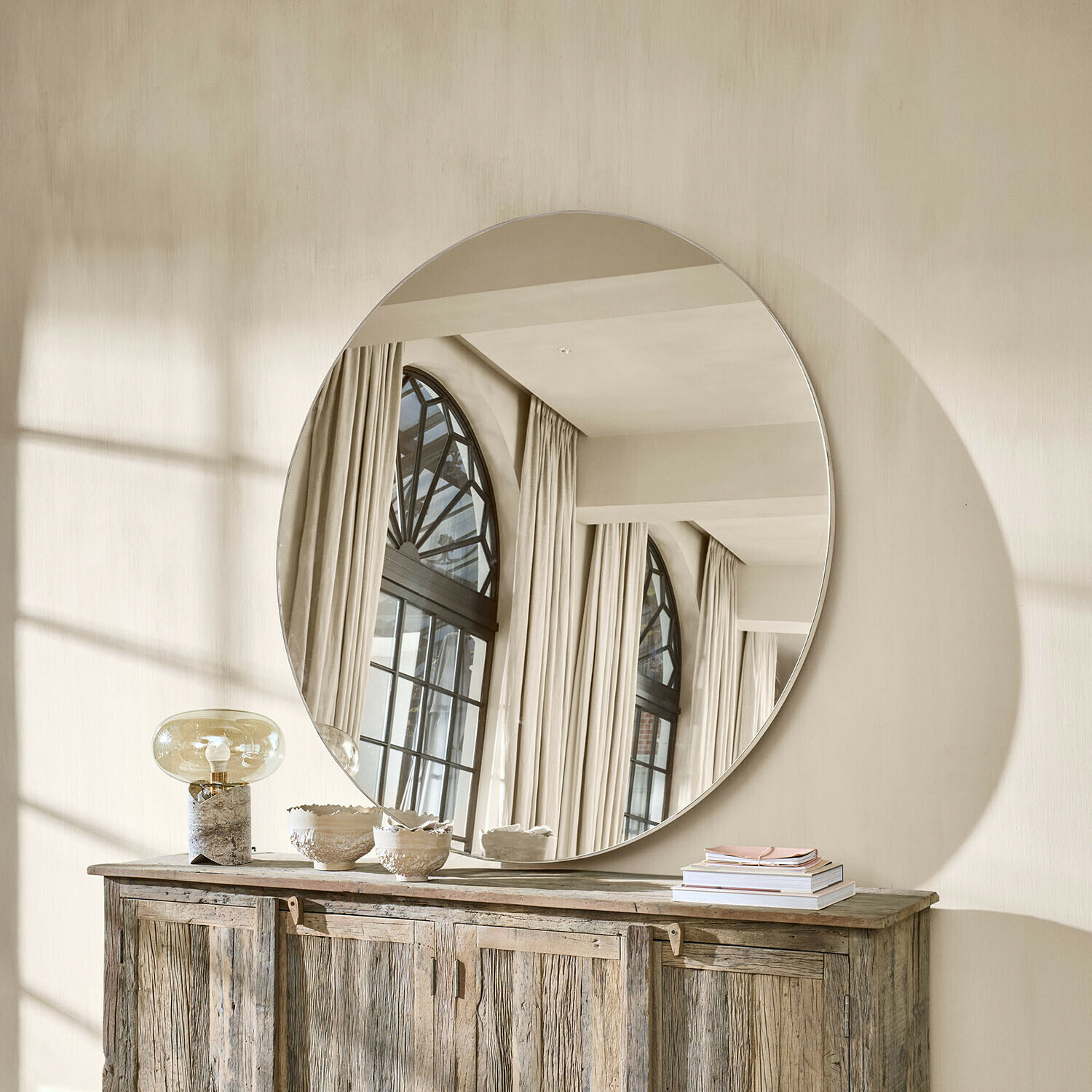 Großer runder Spiegel an der Wand über einem rustikalen Holzsideboard in hellem Raum