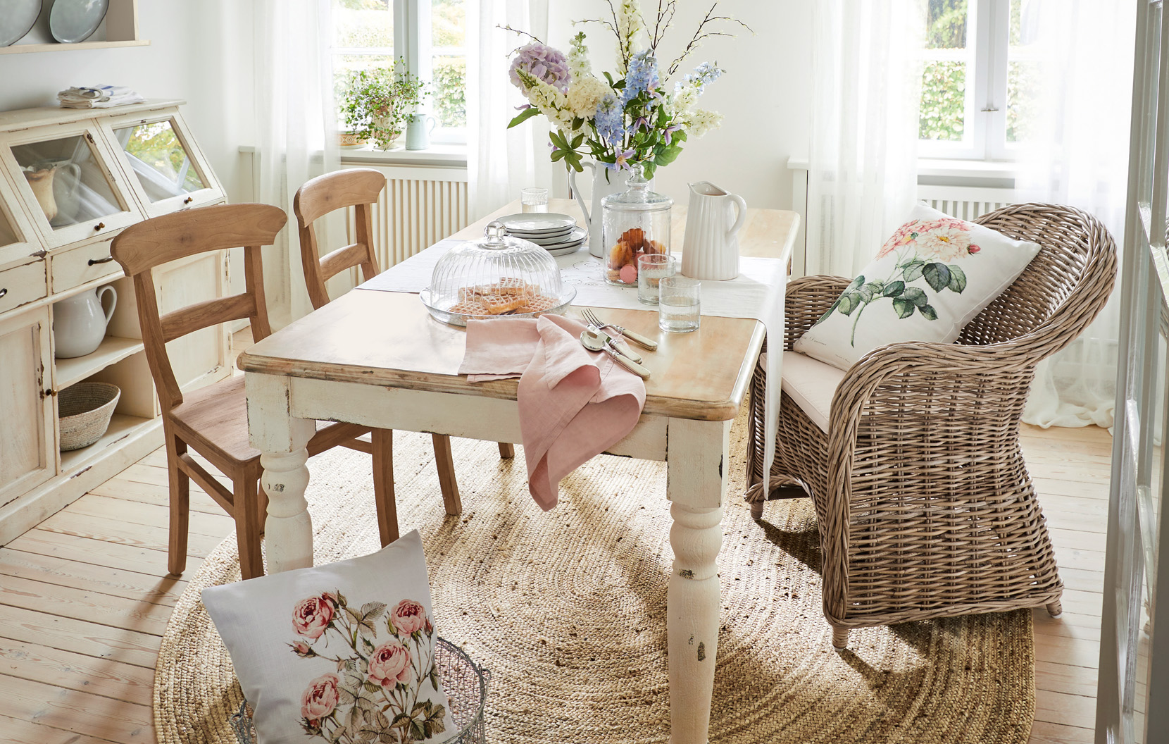 Shabby-Chic-Esszimmer mit Holztisch, Rattansesseln und Blumenarrangement in hellem Raum