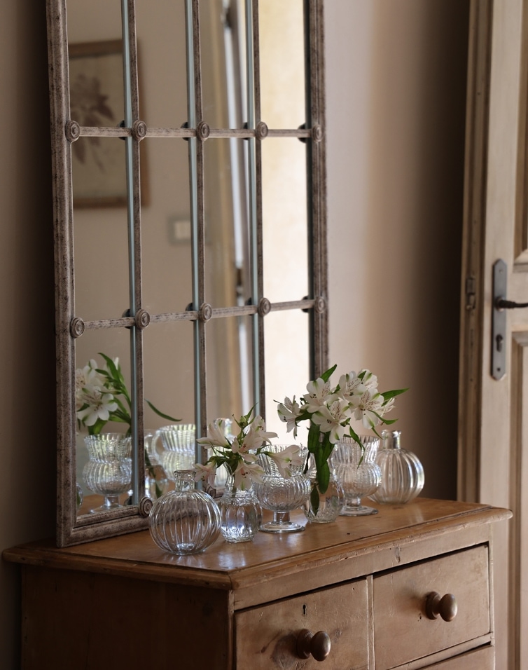 Holzkommode mit Metallrahmen-Spiegel und Glasvasen mit weissen Blumen im Vintage-Stil