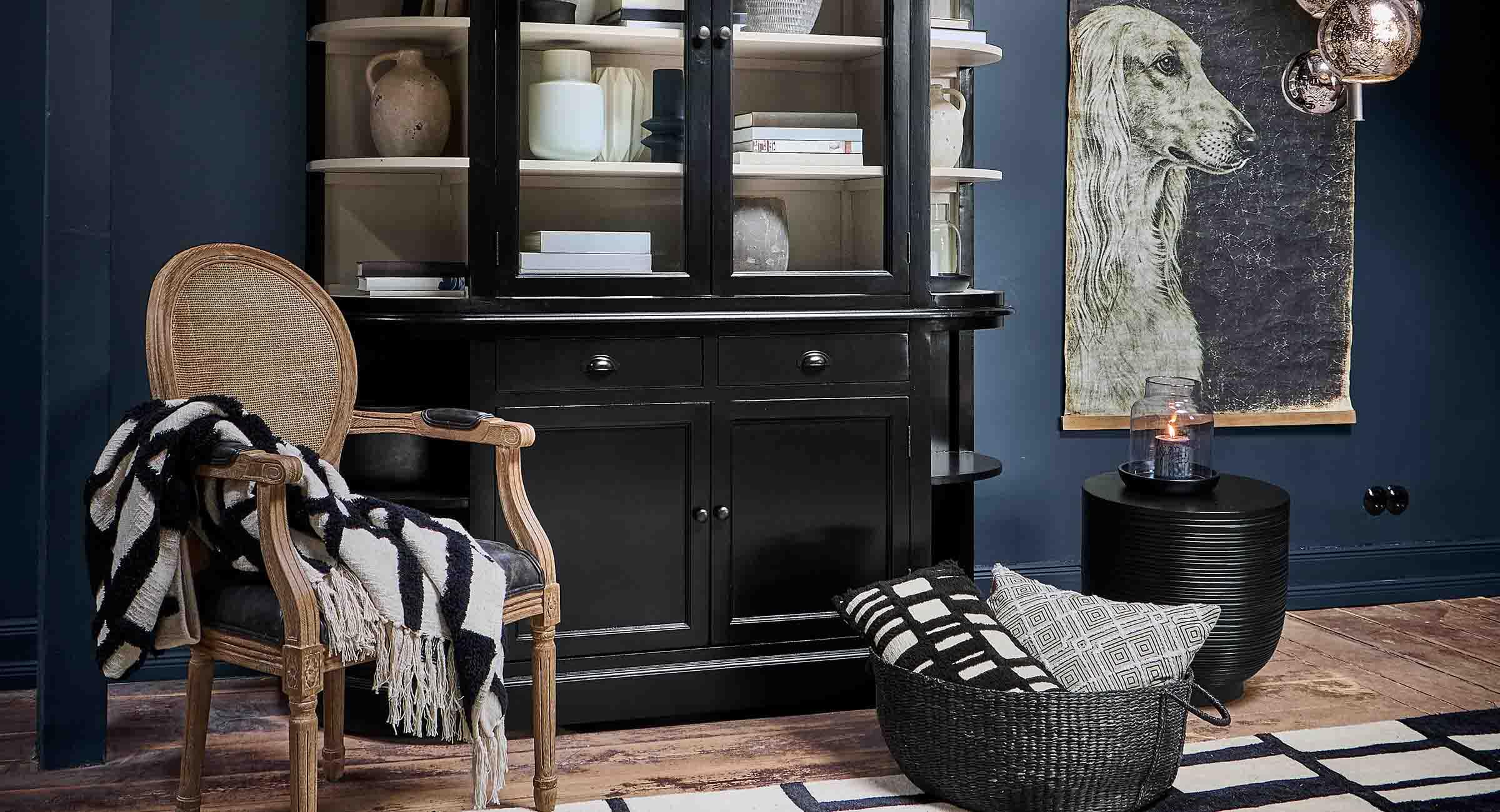 Schwarze Holzvitrine mit Regalen, Naturdekorationen und Korbsessel in elegantem Wohnzimmer