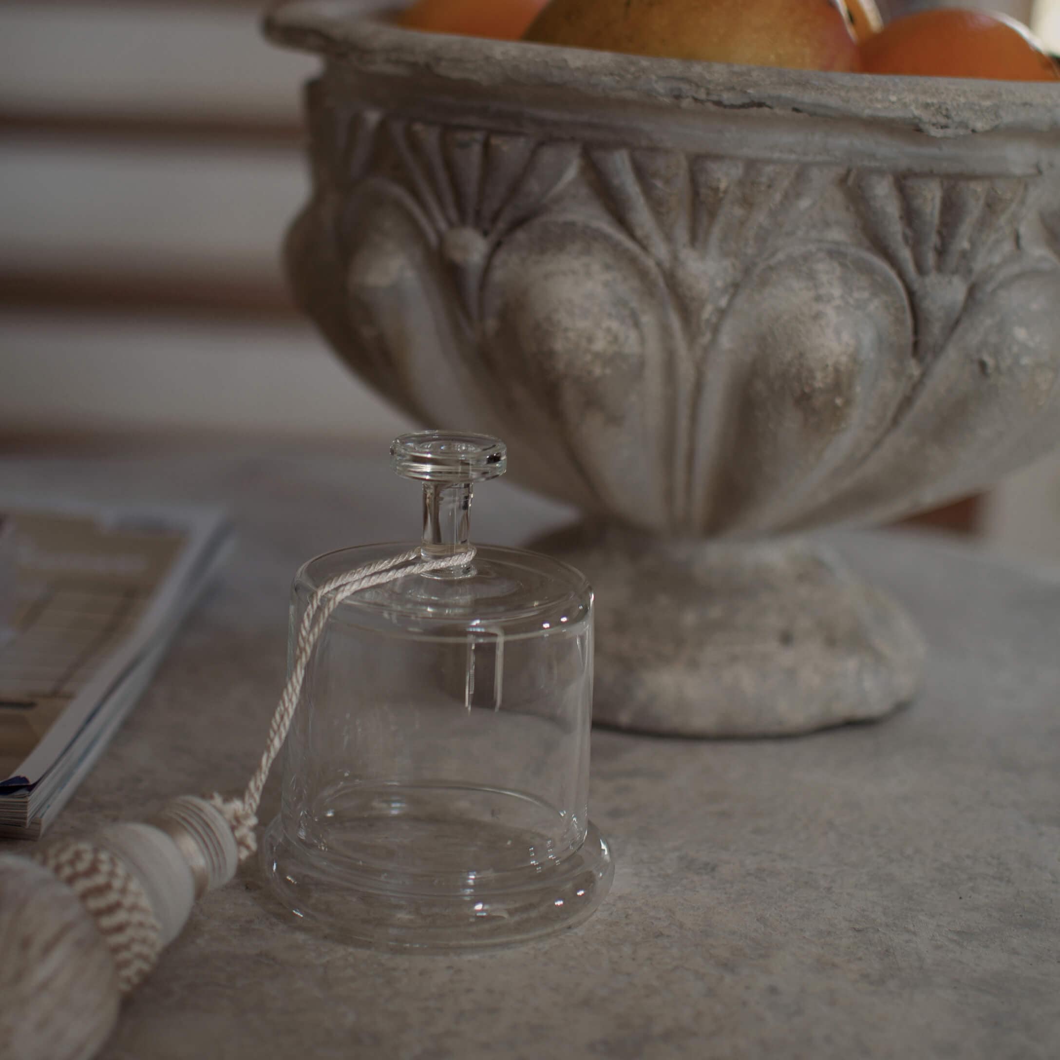 Transparente Glasglocke mit weissem Schnur auf Steintisch neben dekorativer Steinschale