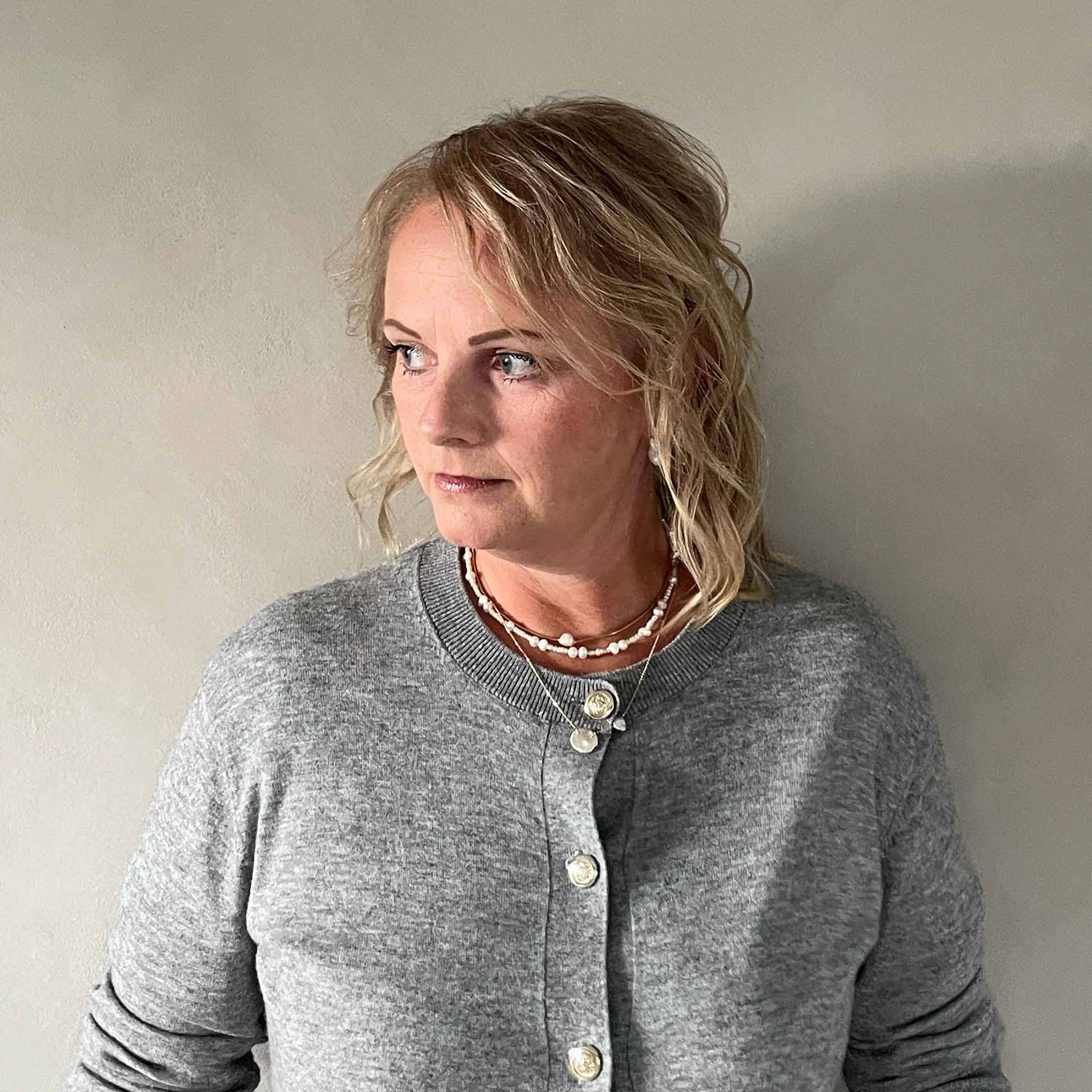 Frau in grauem Pullover mit Knöpfen und Halsketten vor hellem Hintergrund, legerer Stil
