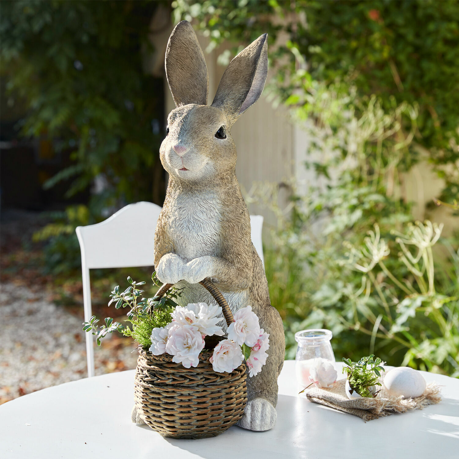 Hase mit Pflanzkorb Alais Dekoratives Kaninchen aus Kunststoff mit Weidenkorb und weissen Blumen auf dem Gartentisch