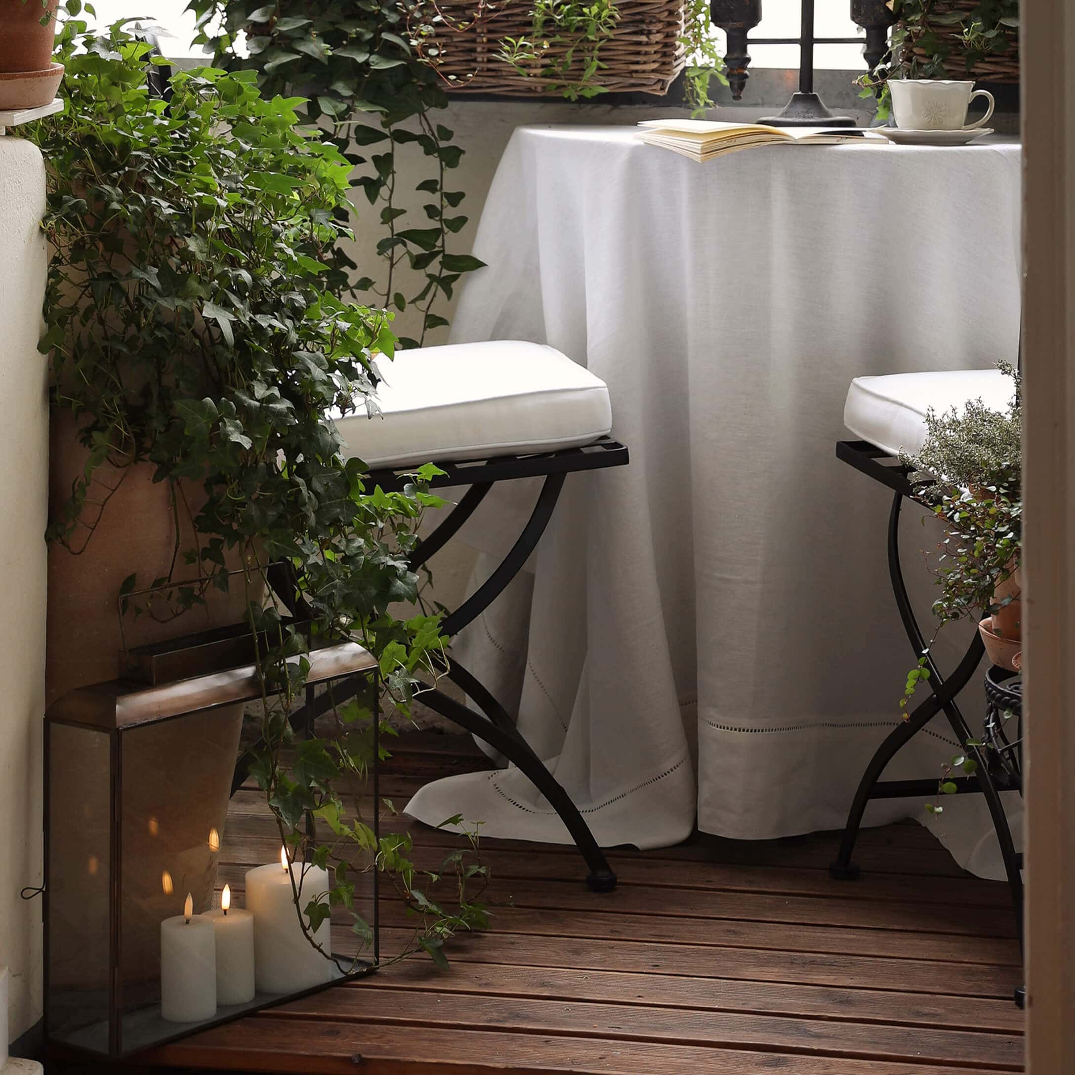 Gemütlicher Balkon mit Holzboden, weissem Tischtuch und Metallstühlen mit weissen Polstern