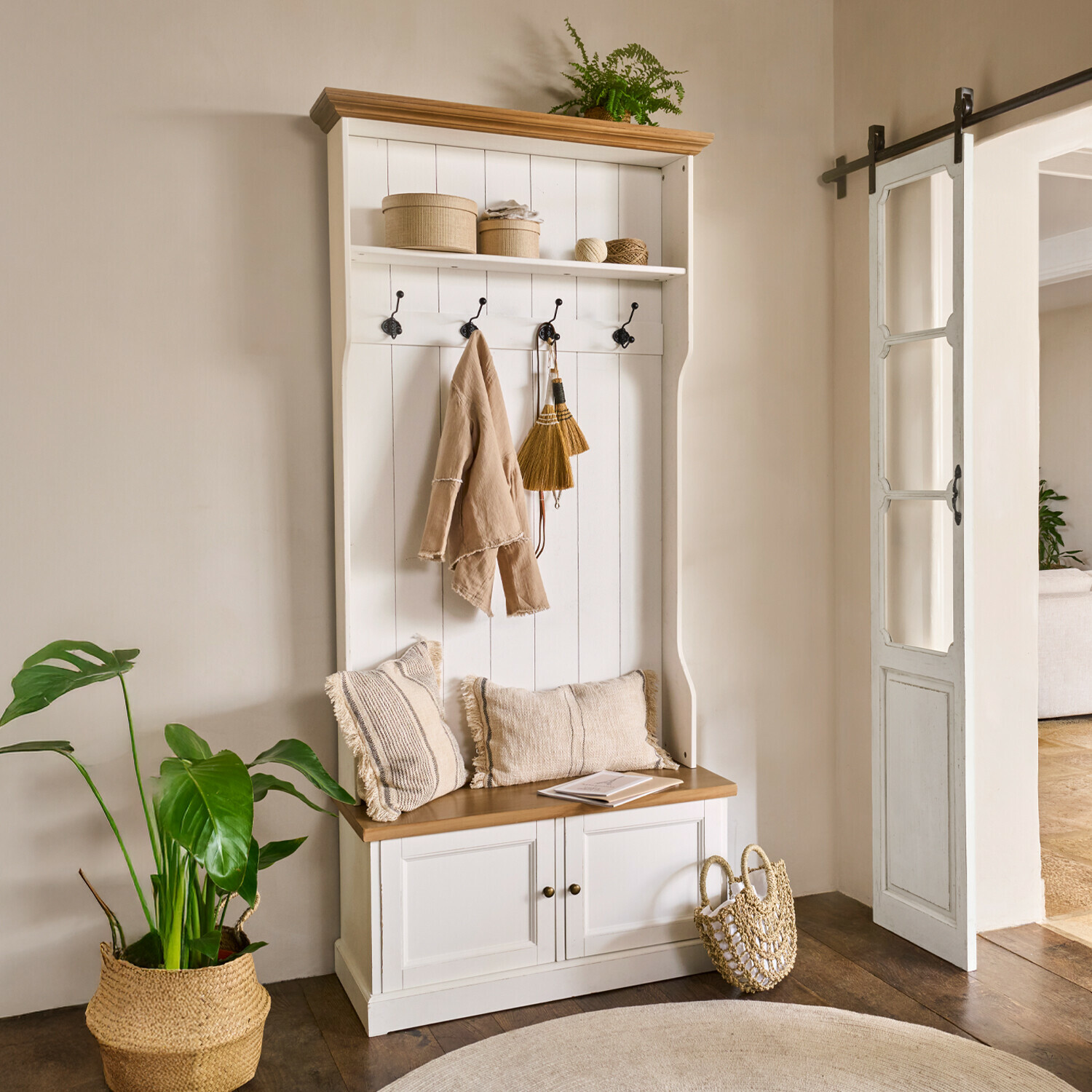 Weiße Holzgarderobe mit Sitzbank, Haken, beigen Kissen und natürlichen Dekorationen im Eingangsbereich
