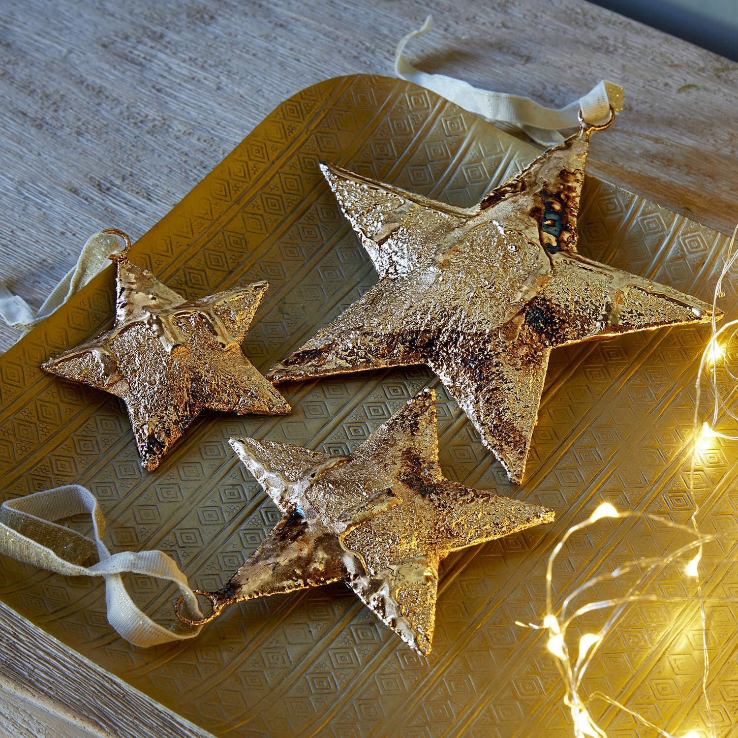 Anhänger 3er Set Myrska Drei goldene Metallsterne als Dekoration auf goldfarbenem Tablett mit LED-Lichterkette