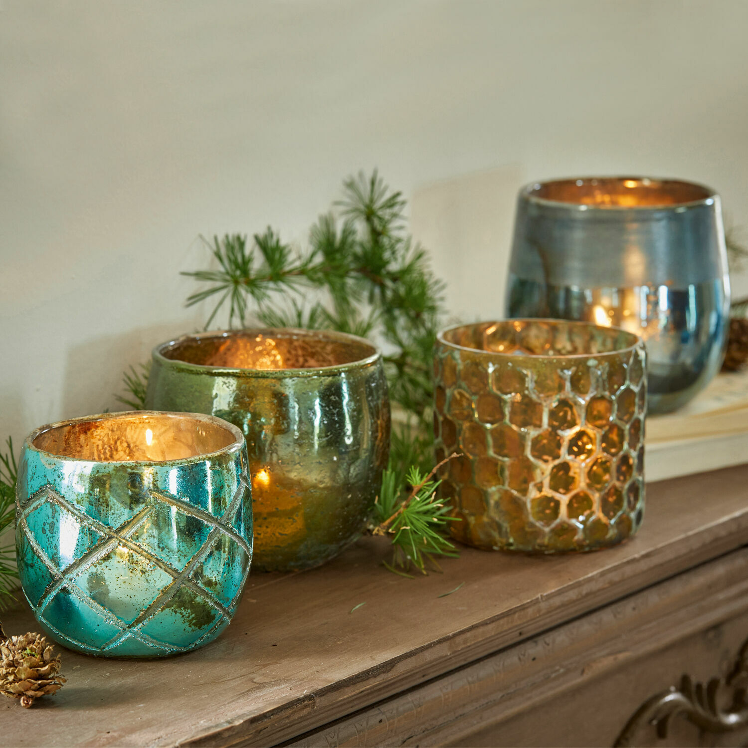 Windlicht 4er Set Marine Vier bunte Glas-Teelichthalter in Türkis, Grün und Gold auf einem Holzbrett arrangiert