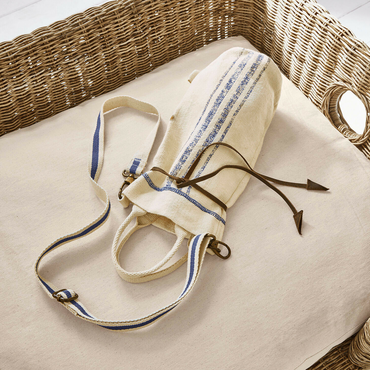 Flaschentragetasche Pawera Beige Baumwolltasche mit blauen Streifen und Lederkordel auf hellem Kissen mit Korbgeflecht